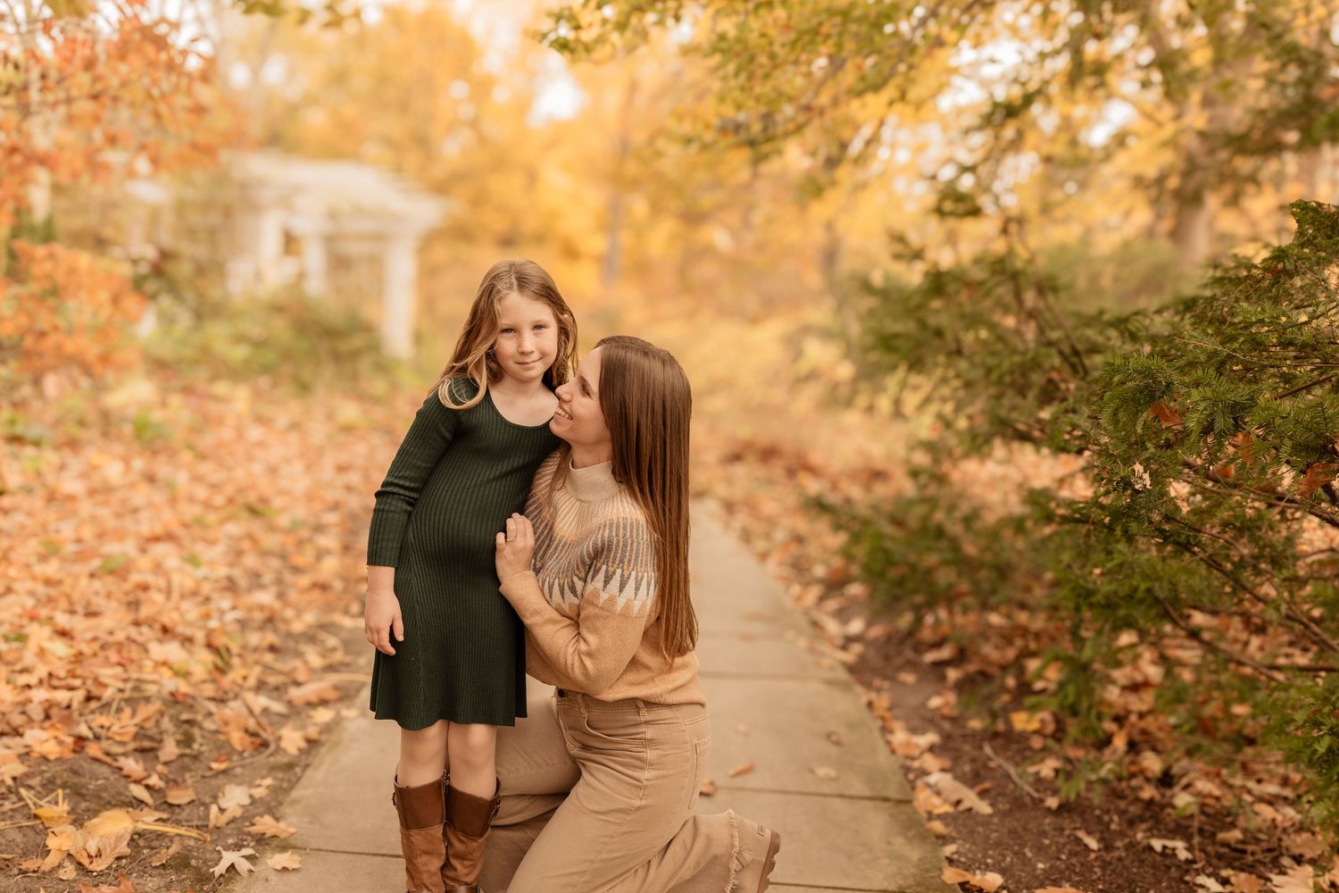 Family members enjoy a tender moment while walking along a leaf-covered path in warm autumn light.