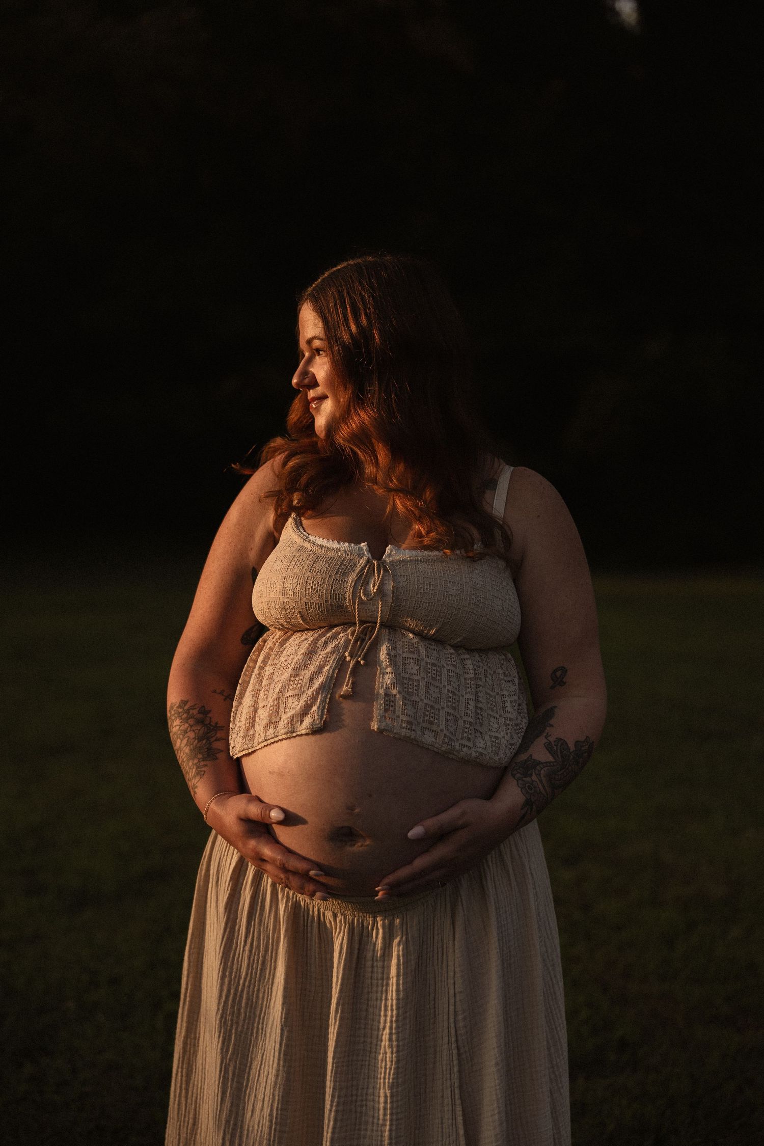 A maternity portrait at golden hour showing an expectant mother in a lace dress.