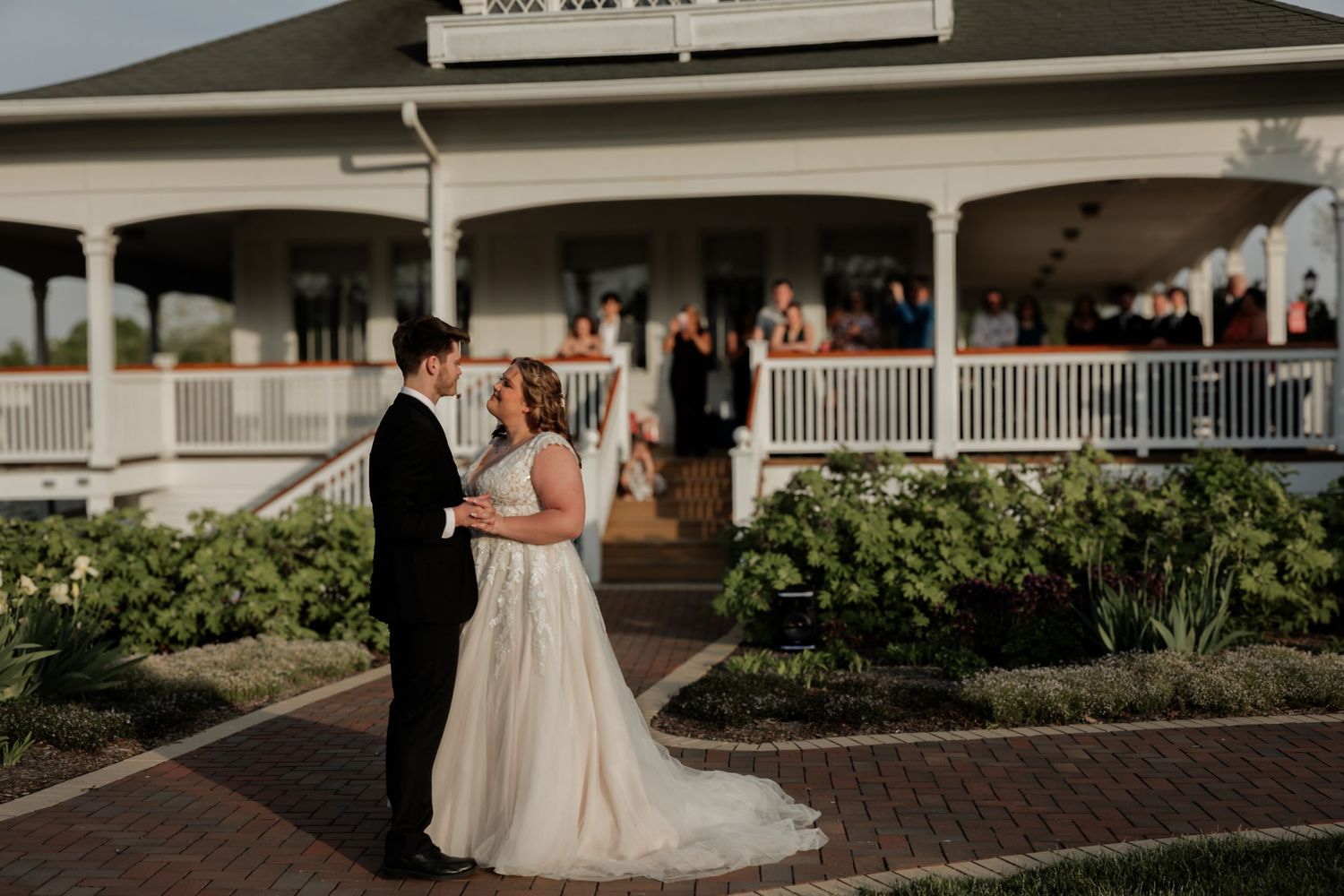 Wedding couple walks along brick pathway outside venue with white columns.