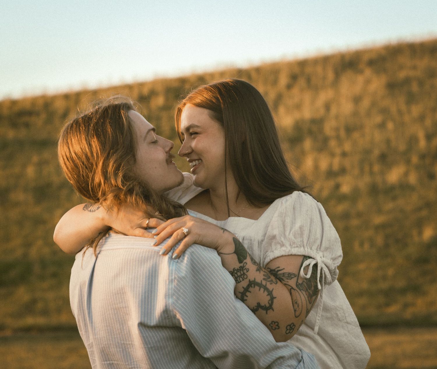 Two women sharing a joyful embrace outdoors at golden hour, one with a floral tattoo on her arm.
