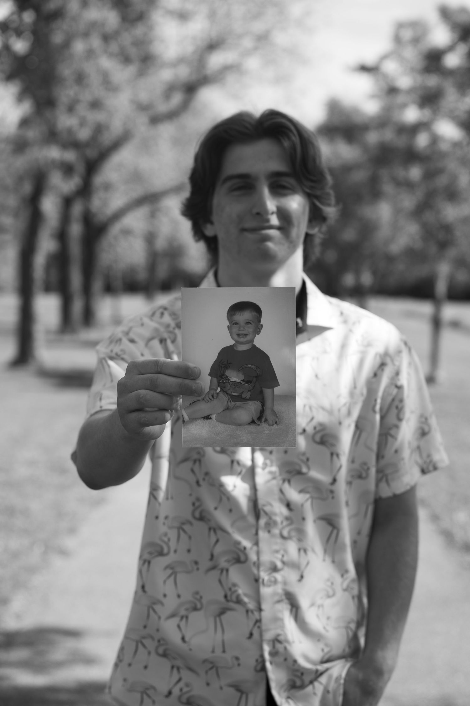 Young man holding a childhood photo of himself outdoors in a park, black and white portrait photography.