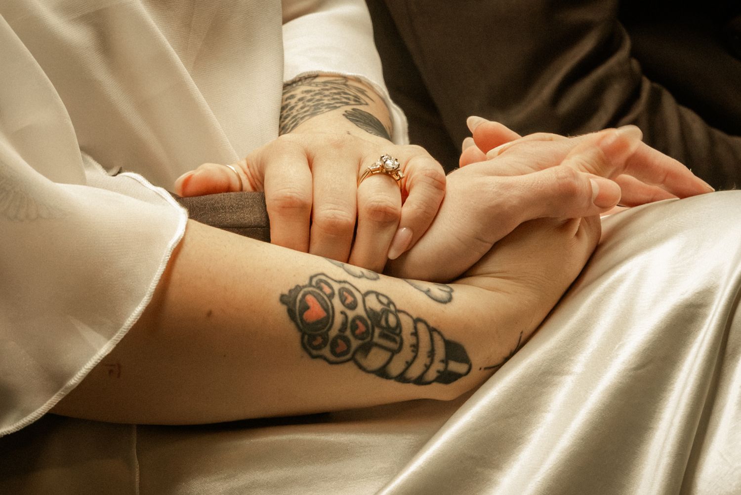 Close-up of couple holding hands, one with colorful forearm tattoo and diamond engagement ring on wedding day.