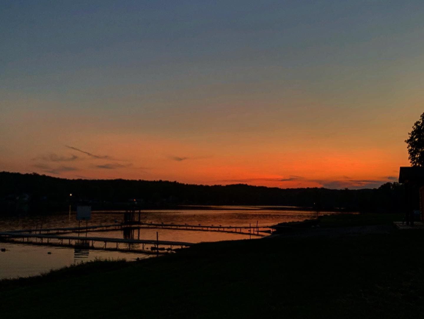 Drone shot capturing a stunning orange and blue sunset over a dark silhouetted coastline with bridge in the distance.