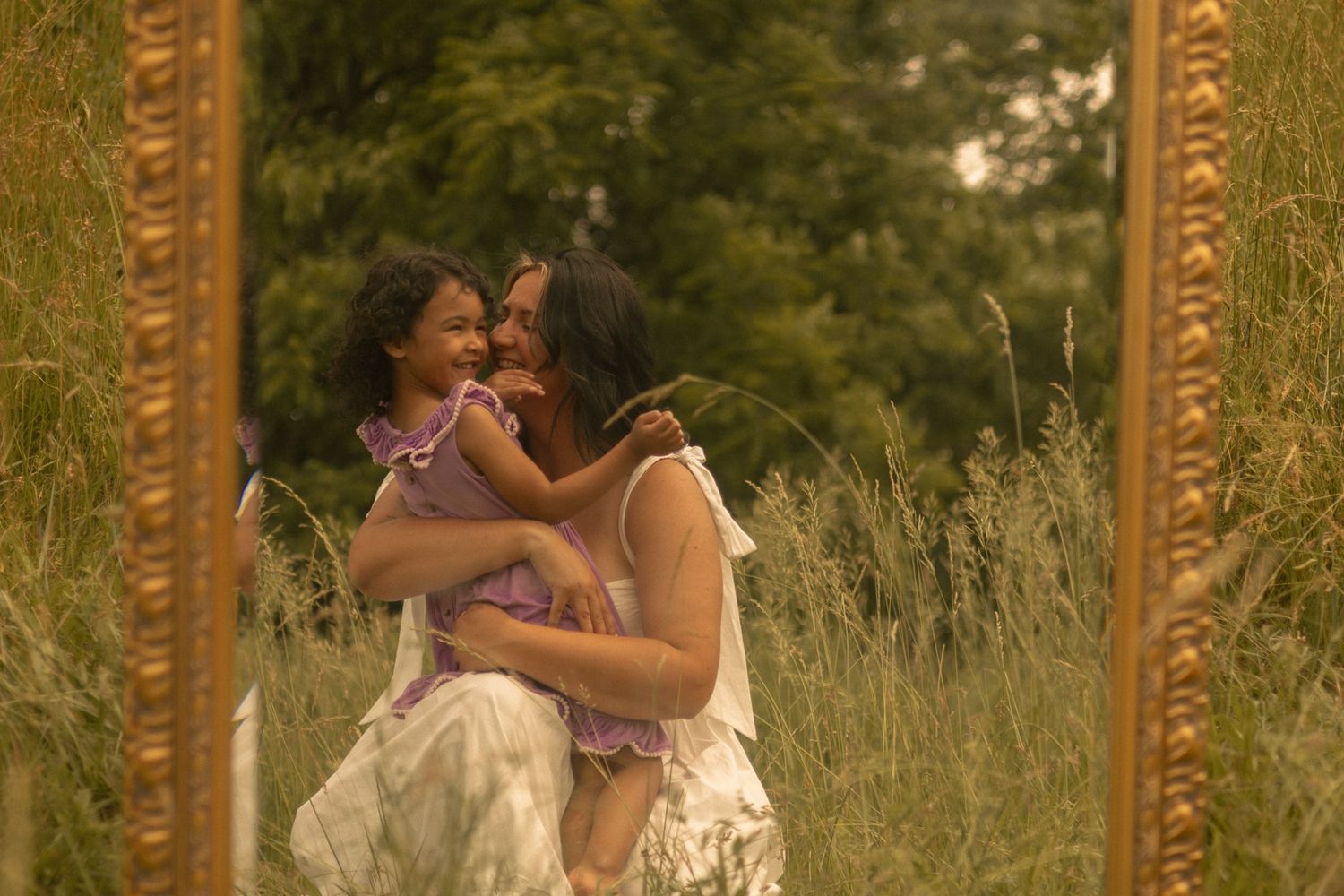 a mother and daughter embrace with love in an outdoor session utilizing a mirror prop for a story telling aspect