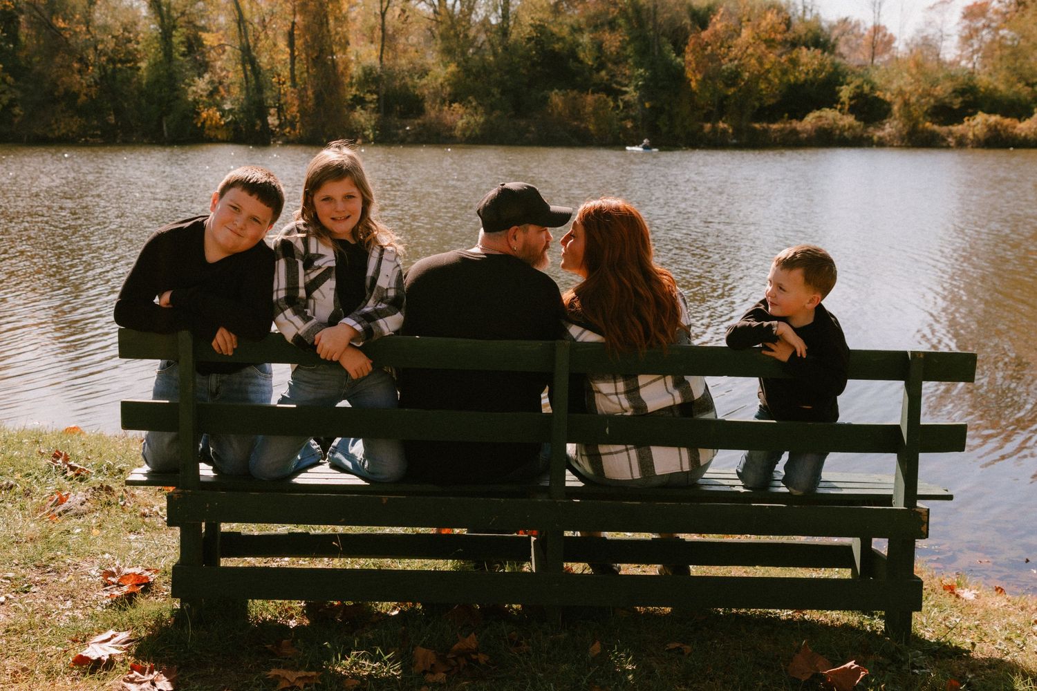 Group sits together on wooden bench by lake during fall sunset photoshoot.