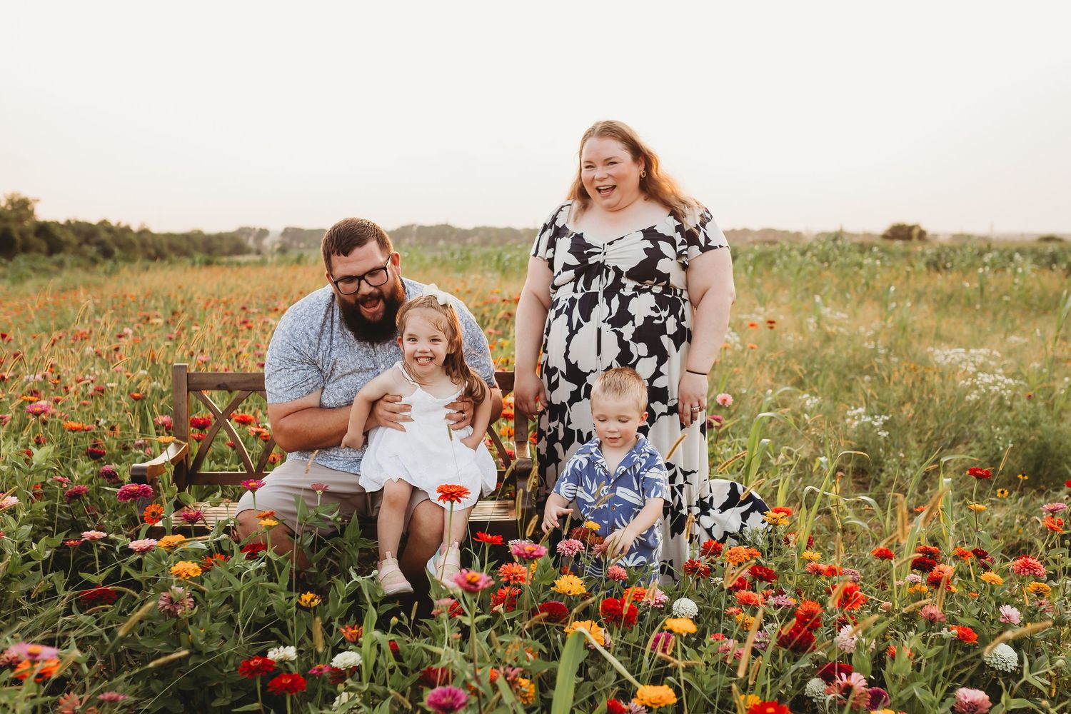 Family of four posing in vibrant colorful flower field at dusk with young children.