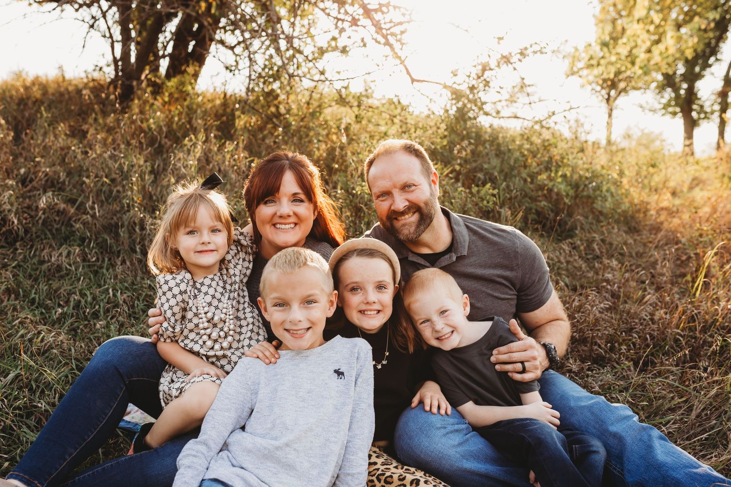 Smiling family of six posing together outdoors in warm golden fall light.