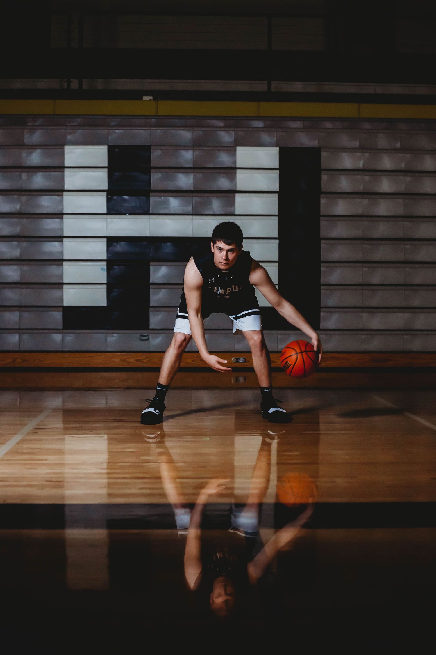 Young male basketball player dribbling on a glossy hardwood court with his reflection visible below.