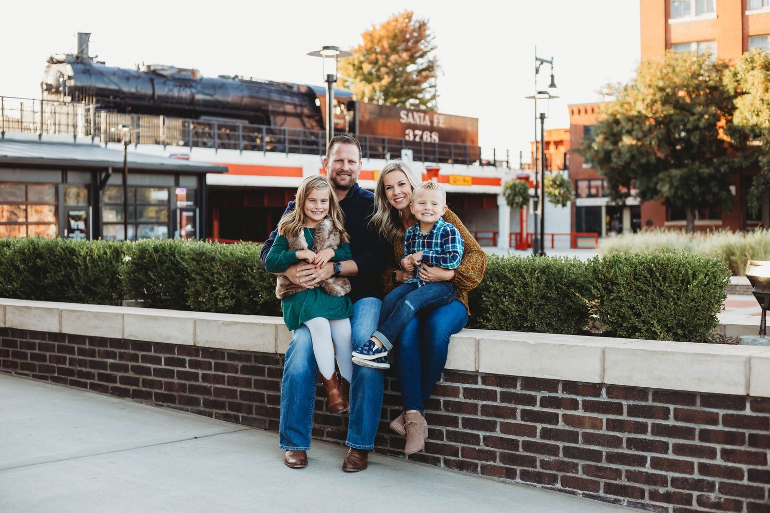 Happy family of four sitting on brick wall in urban setting during fall season.