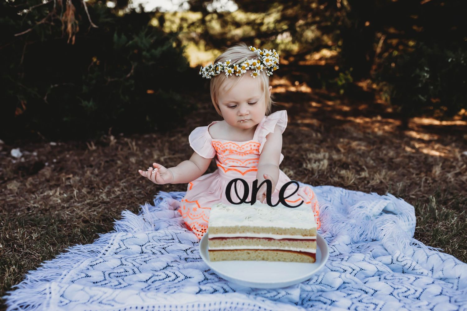 Baby girl in pink dress with floral crown smiles at first birthday cake smash with \