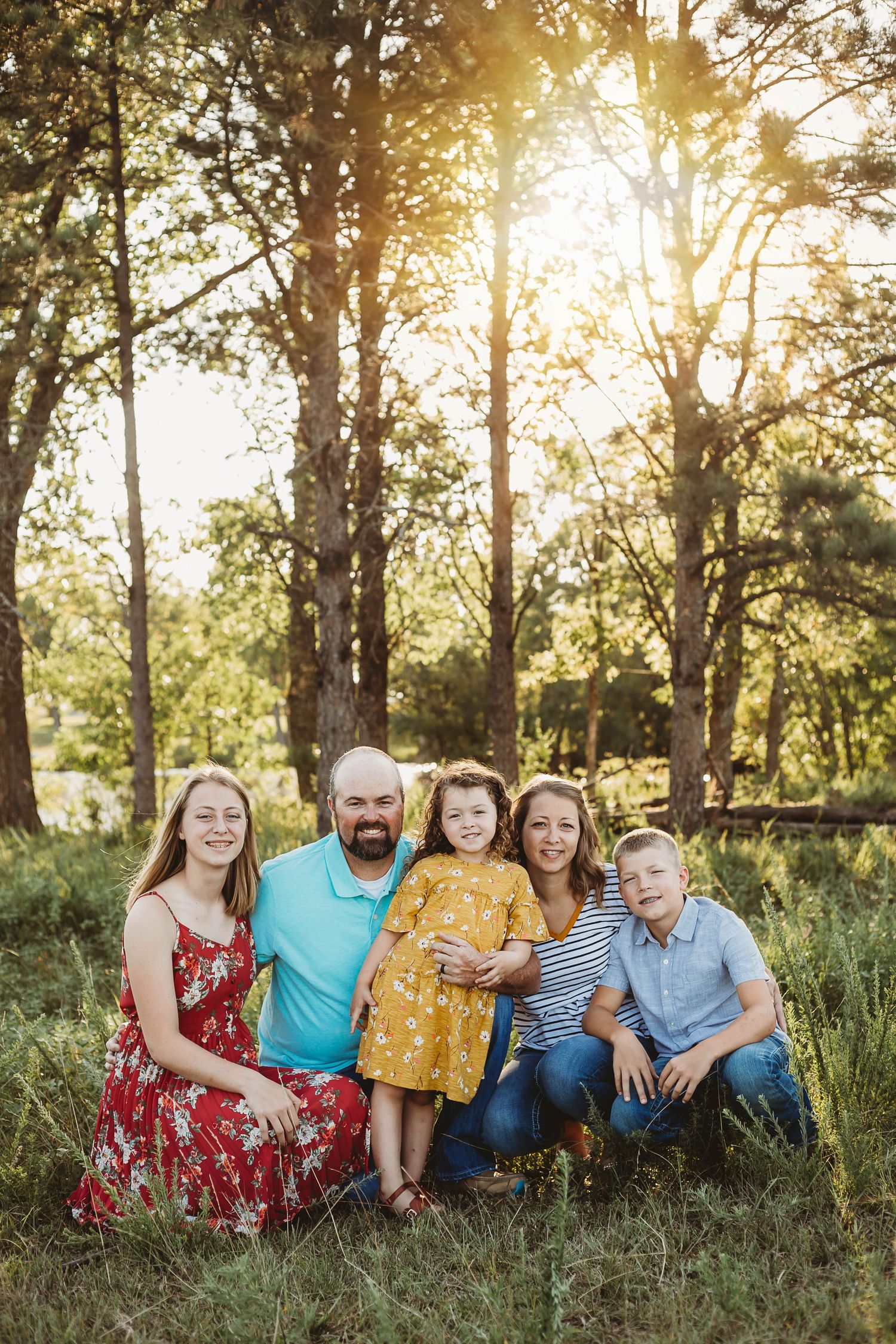 Happy family of five posing together in sunlit forest meadow for outdoor portrait session.