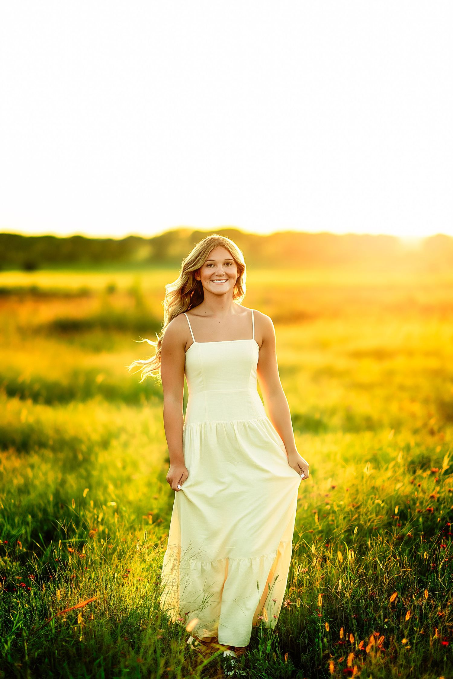 Young woman in white sundress walking through golden sunlit meadow, smiling joyfully with hair flowing in the breeze.