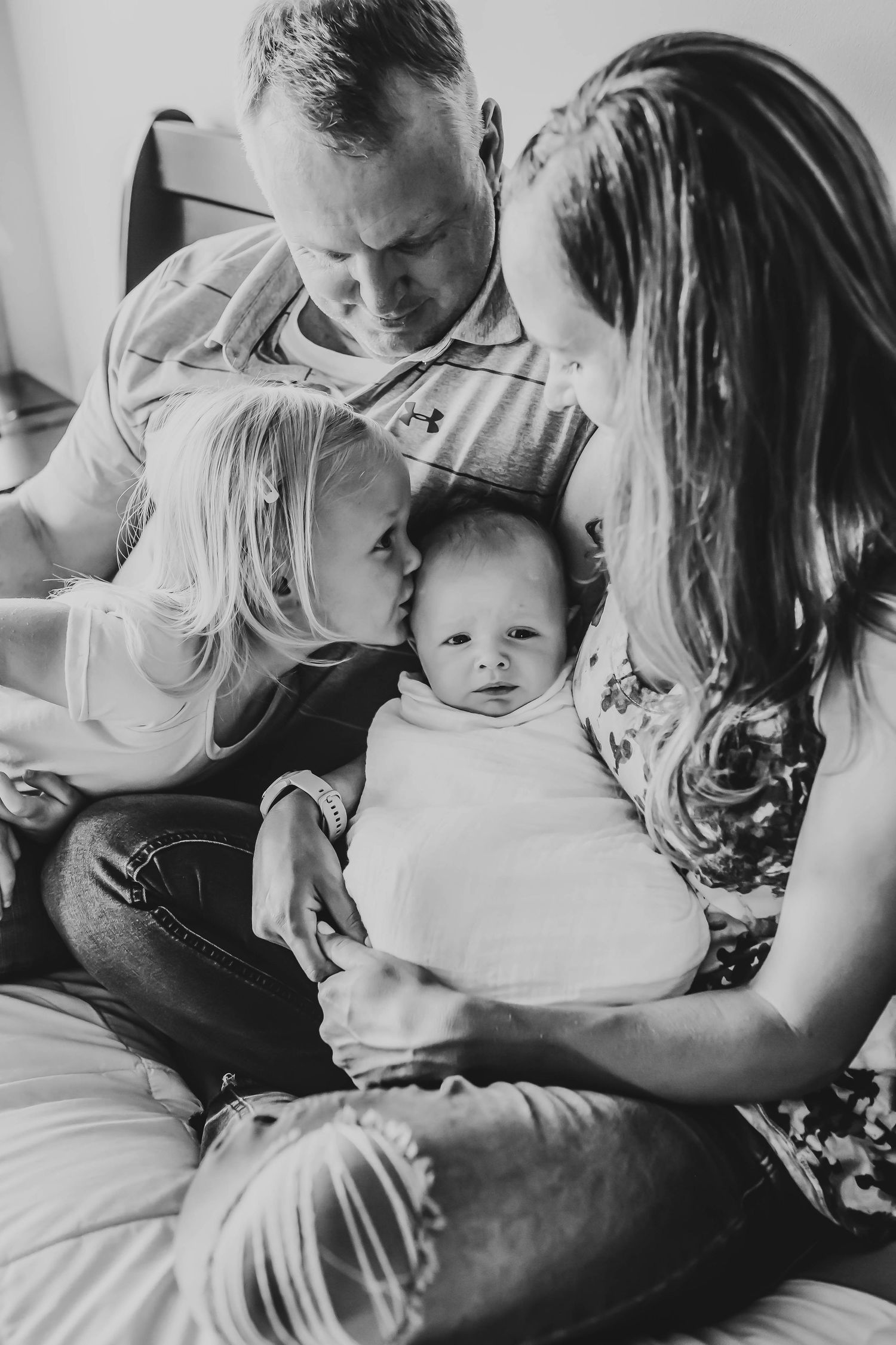 Black and white photo of a family lovingly gathered around their newborn baby.