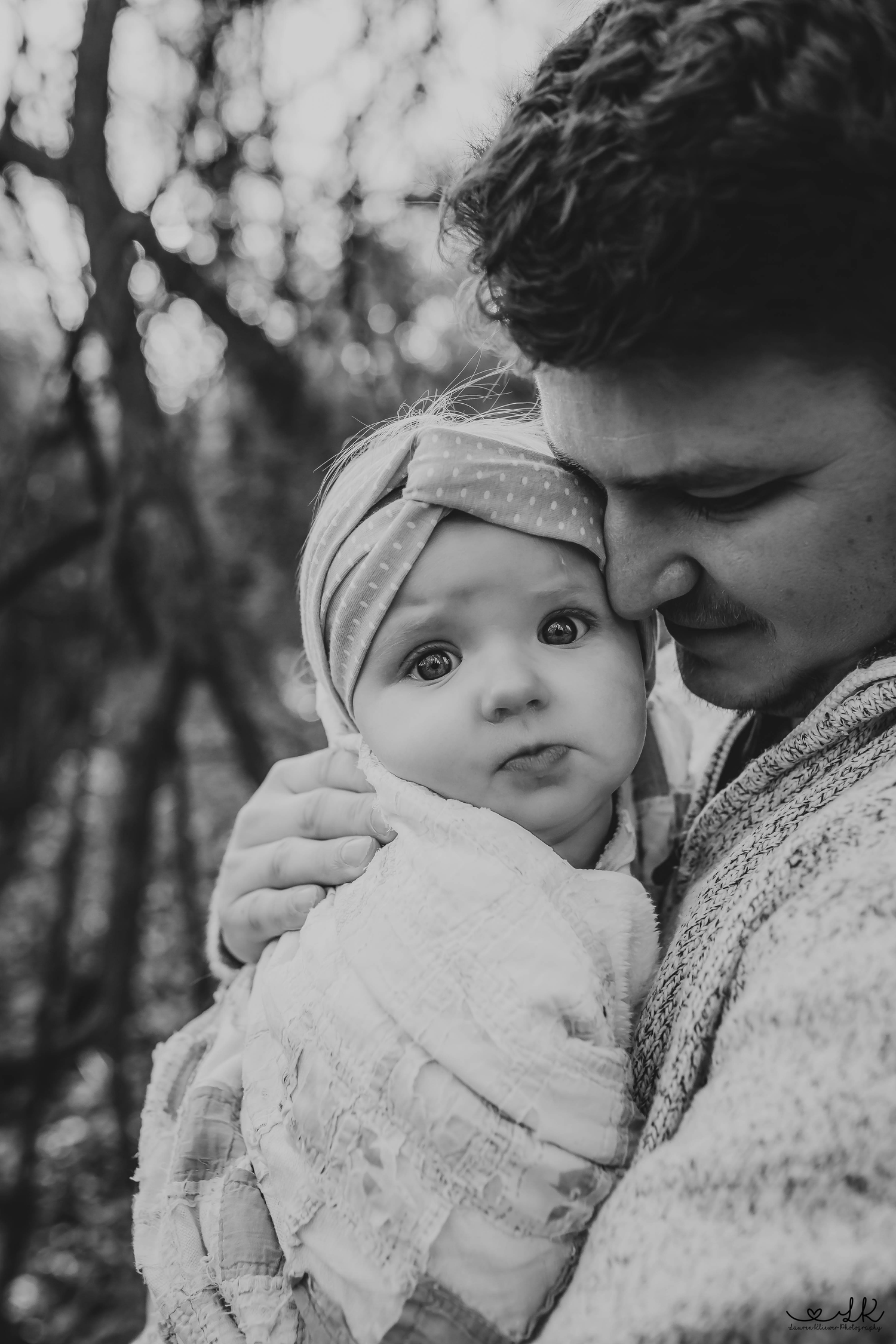 A tender black and white portrait of a father gently holding his newborn baby wrapped in a soft blanket.