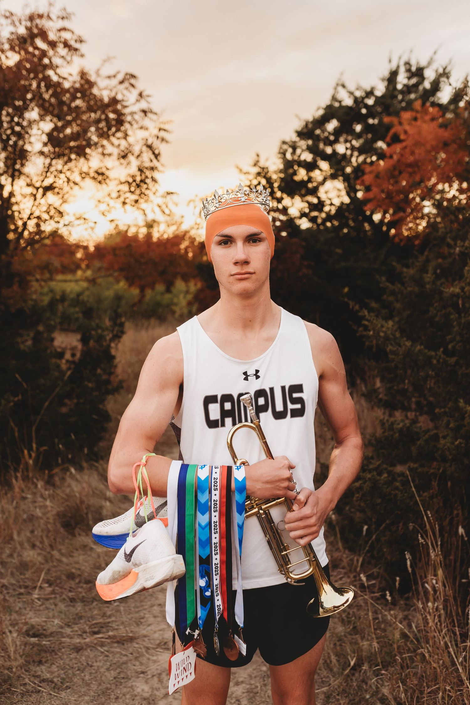 Young athlete in Campus jersey holds trumpet and medals outdoors at sunset, showcasing sports and music achievements.