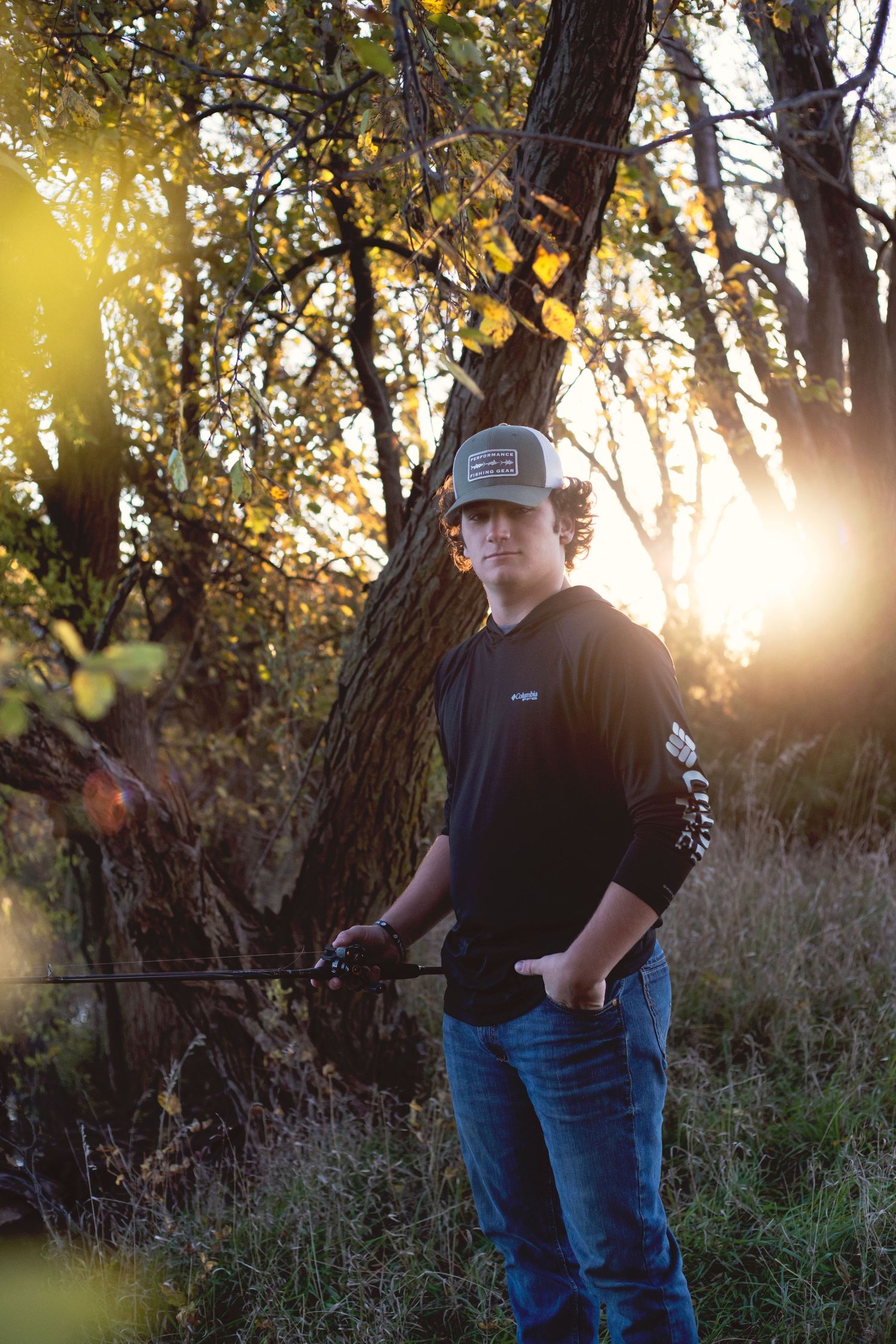 Young man holding a fishing rod at golden hour in an autumn forest setting.