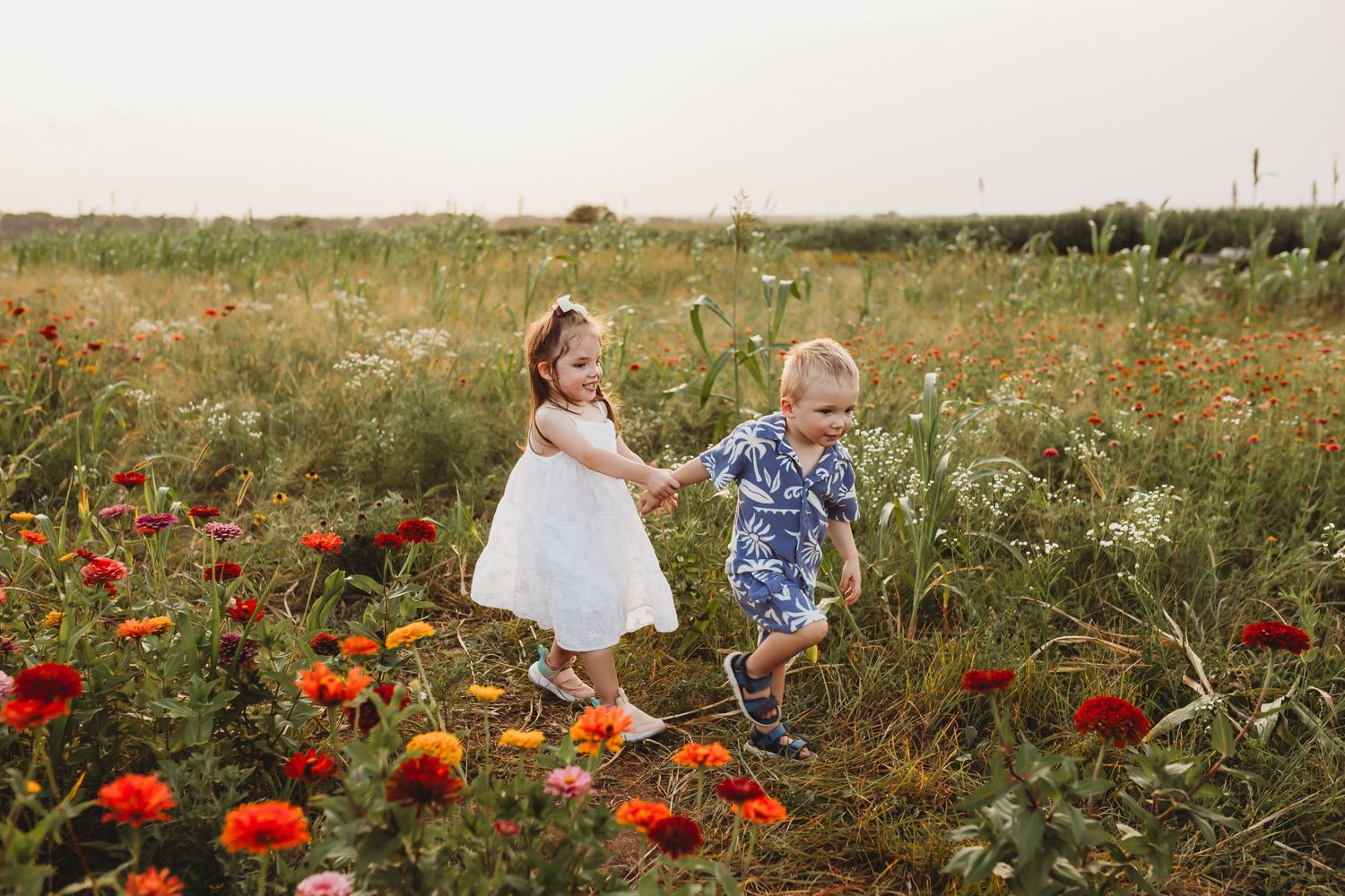 Two young children holding hands while walking through a vibrant wildflower field.