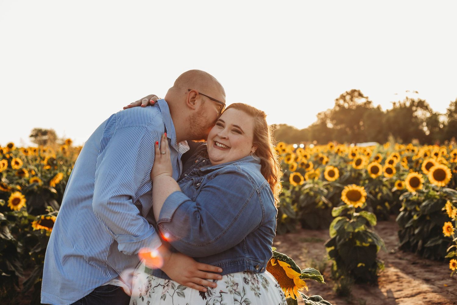 Happy couple embracing and laughing together in a stunning sunflower field during golden hour sunset.