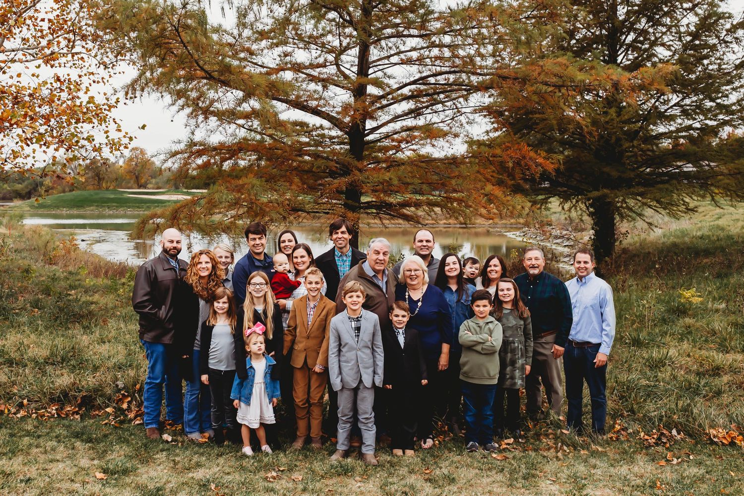 Large extended family group portrait outdoors in autumn with colorful fall foliage and pond.