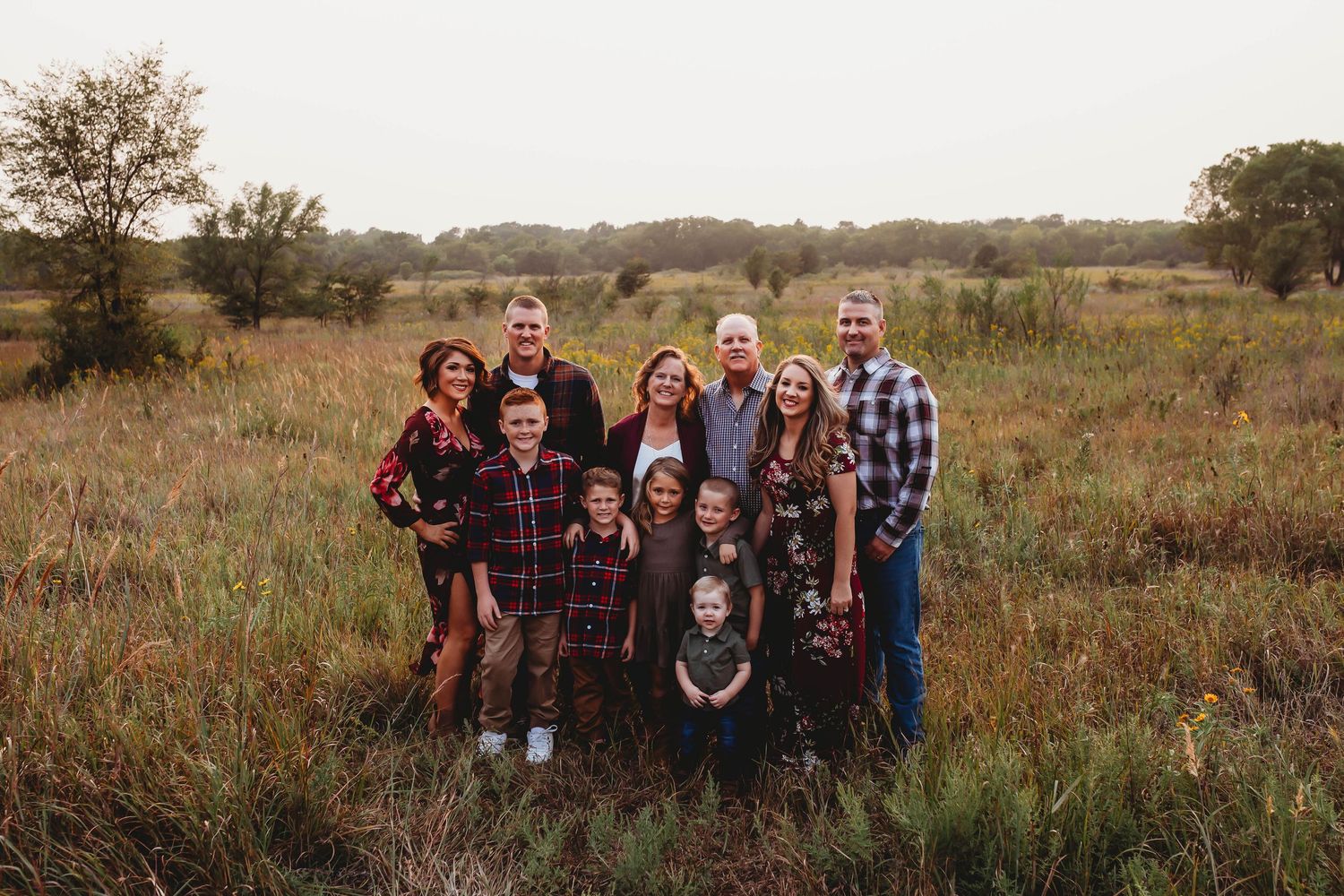 Large extended family posing together in an open autumn meadow at dusk.