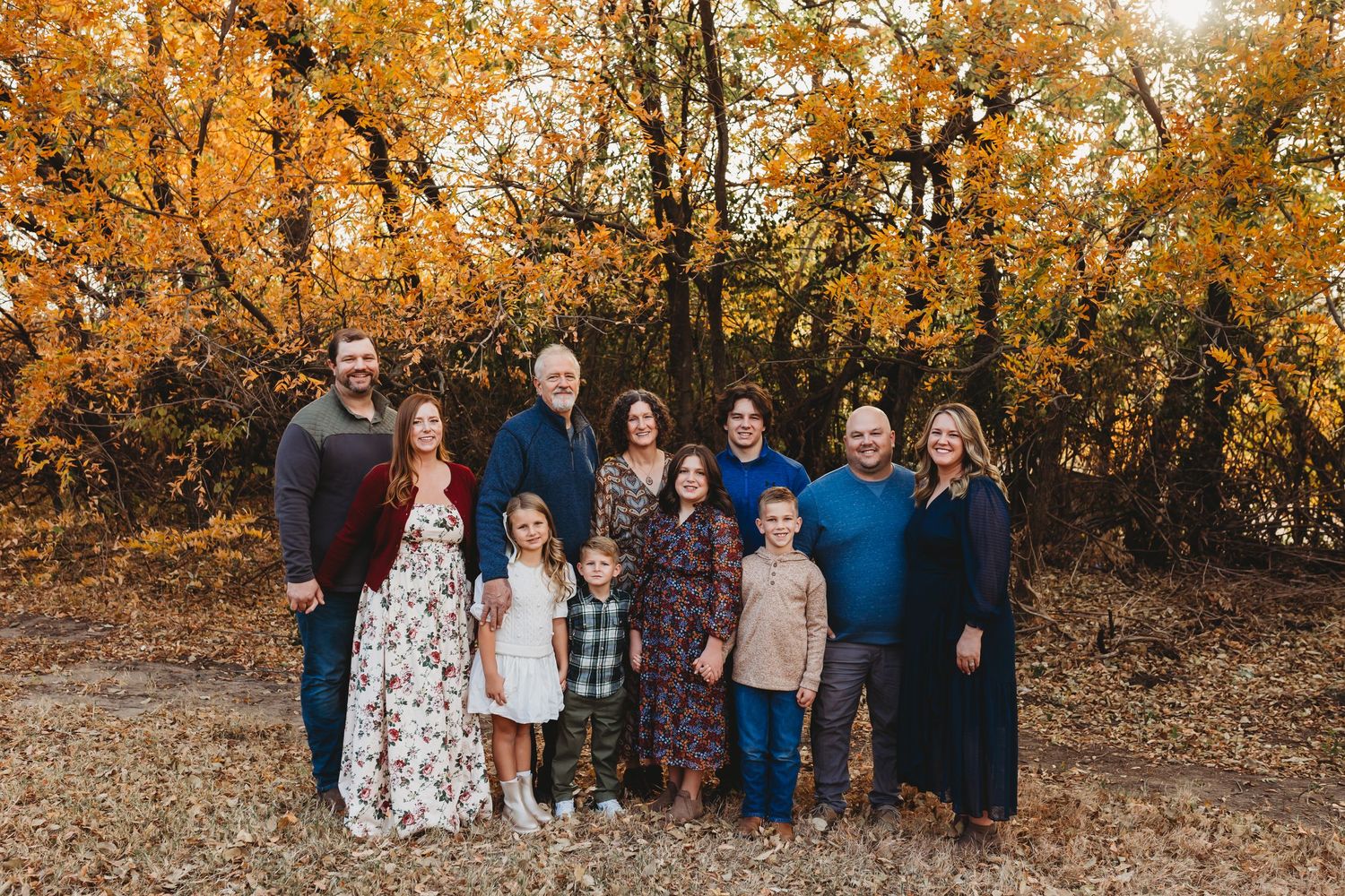 Large extended family of ten posing among vibrant yellow fall foliage.