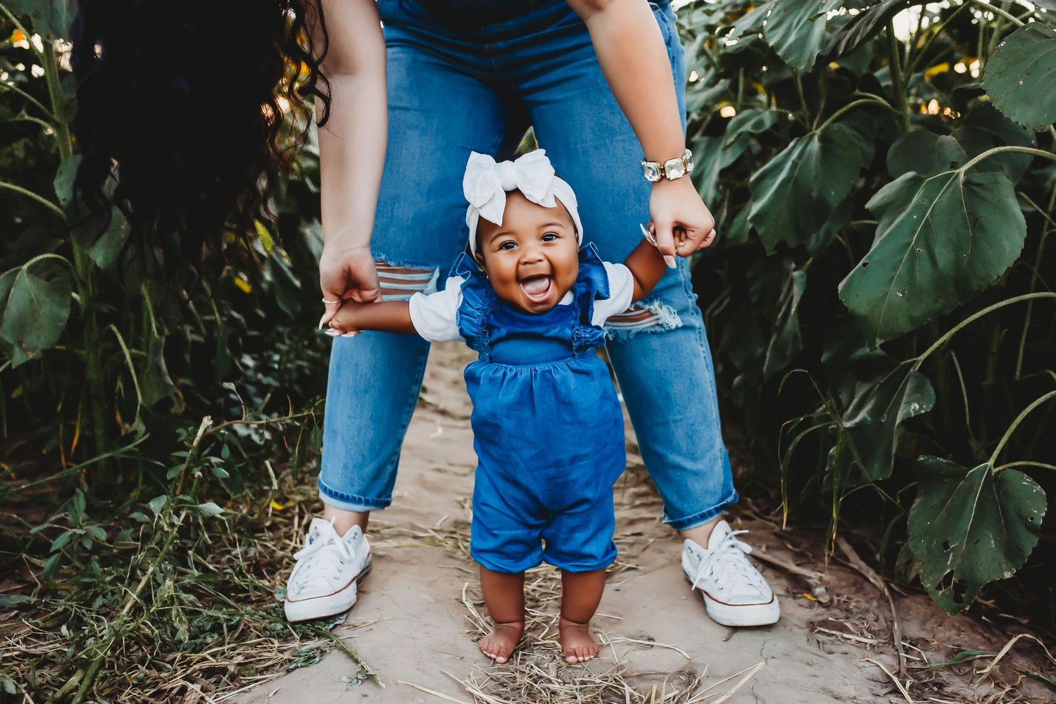 Joyful baby in blue romper learning to walk with parent's support outdoors.