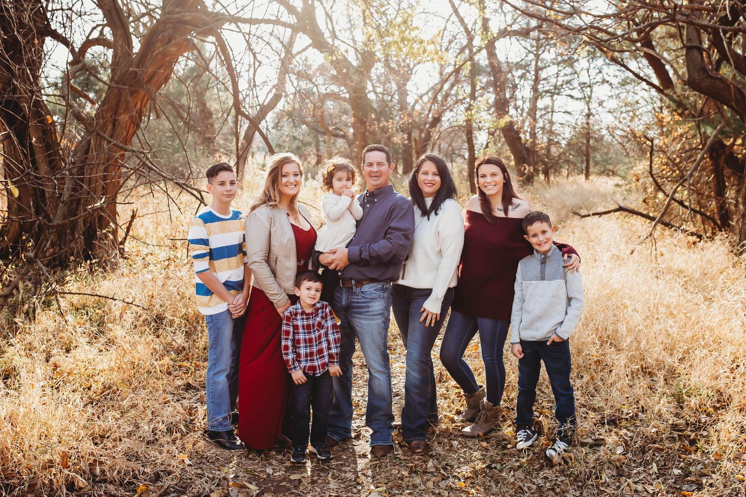 Family of seven posing outdoors among golden trees in fall.
