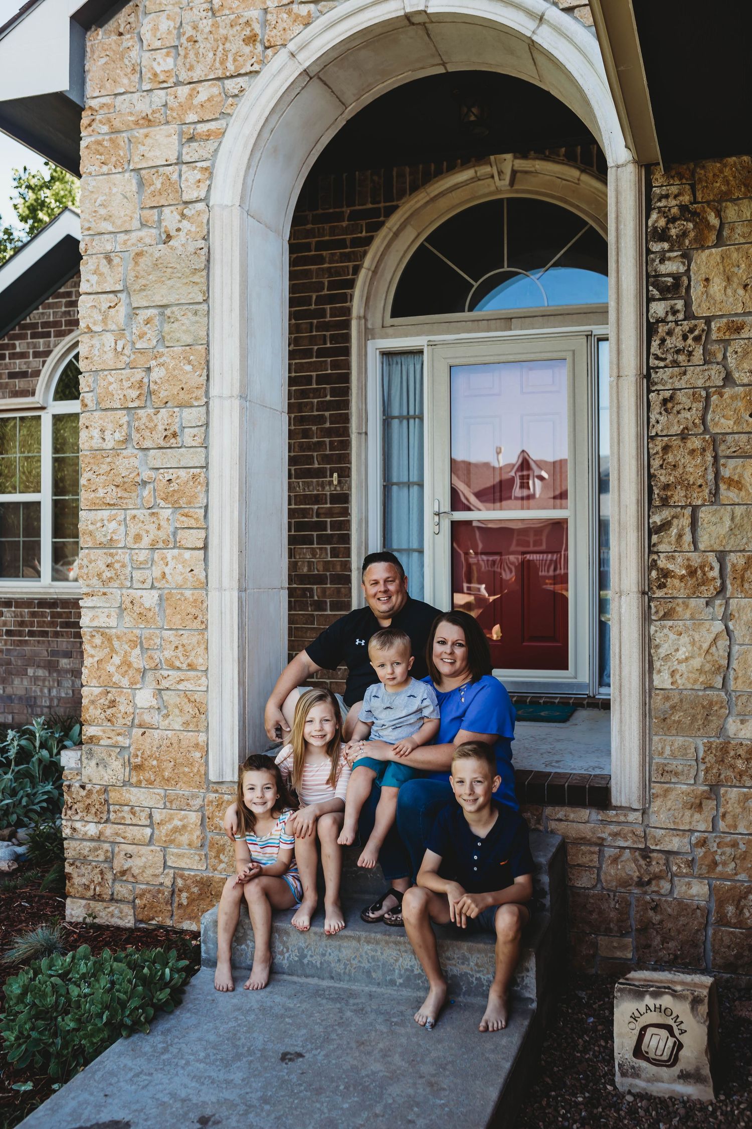 Family of five smiling together on the front porch steps of a brick home.