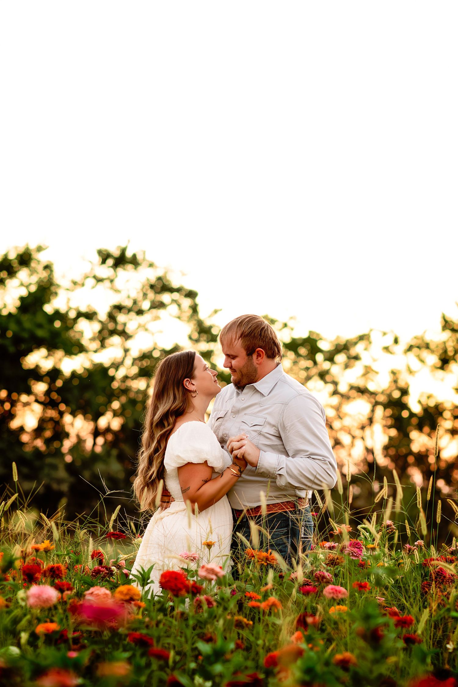 Couple embracing in a wildflower field at golden hour, surrounded by colorful blooms and warm sunset light.