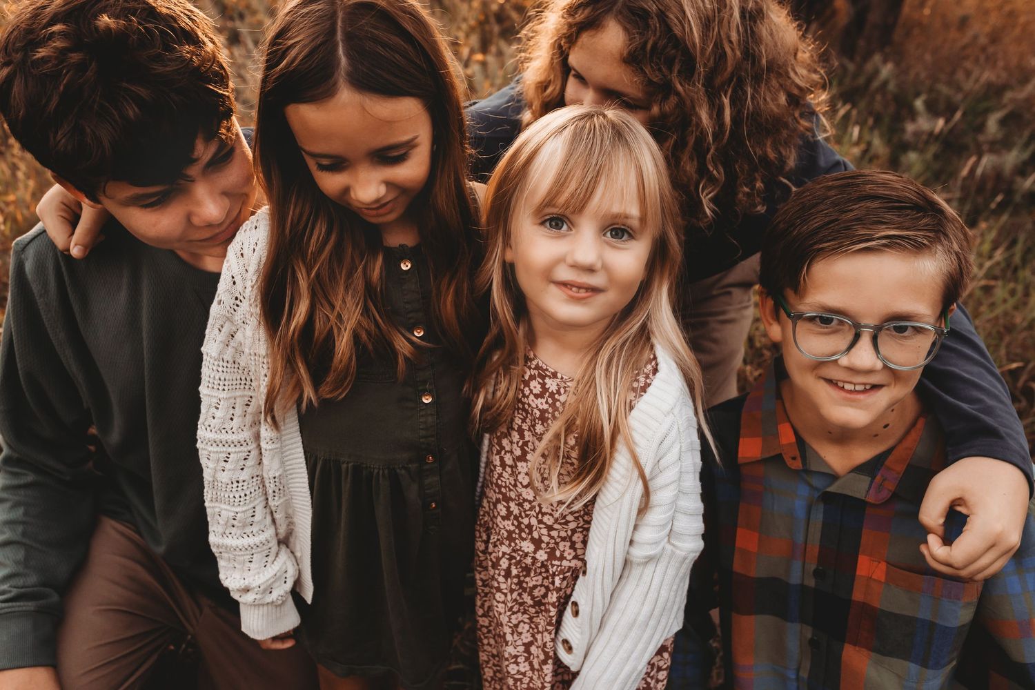 Group of five children smiling and posing together outdoors in a field, wearing casual fall clothing.