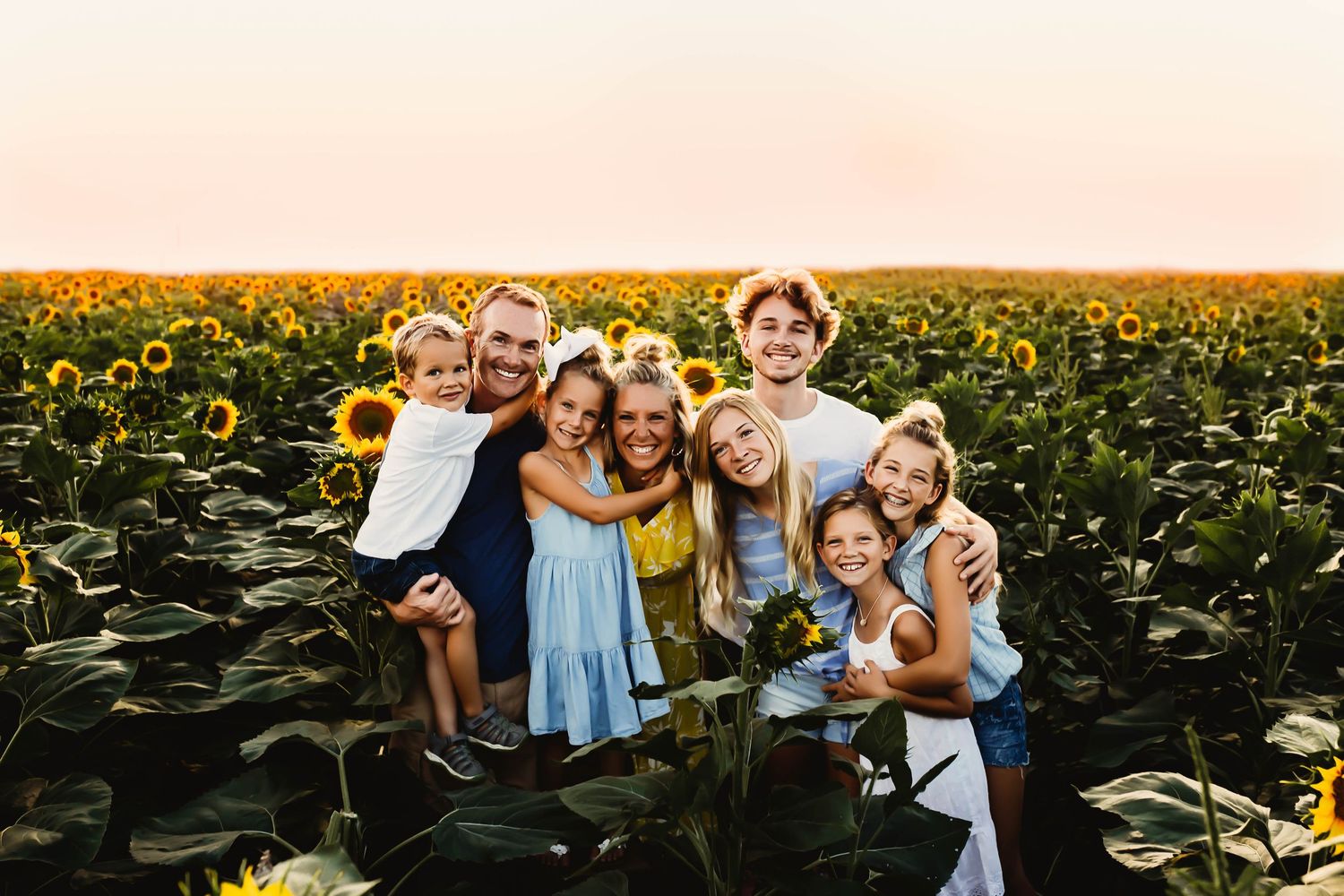 Joyful family of eight smiling together in a vibrant sunflower field at golden sunset.