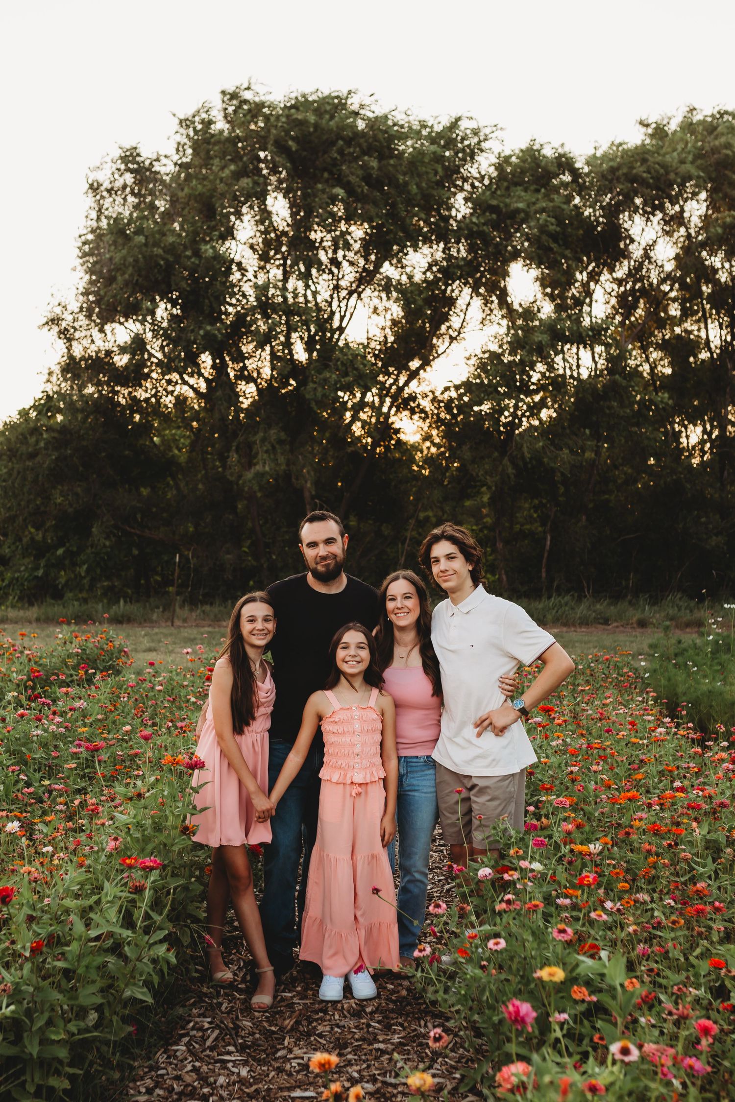 Family of five smiling together in a colorful flower field at golden hour sunset outdoors.