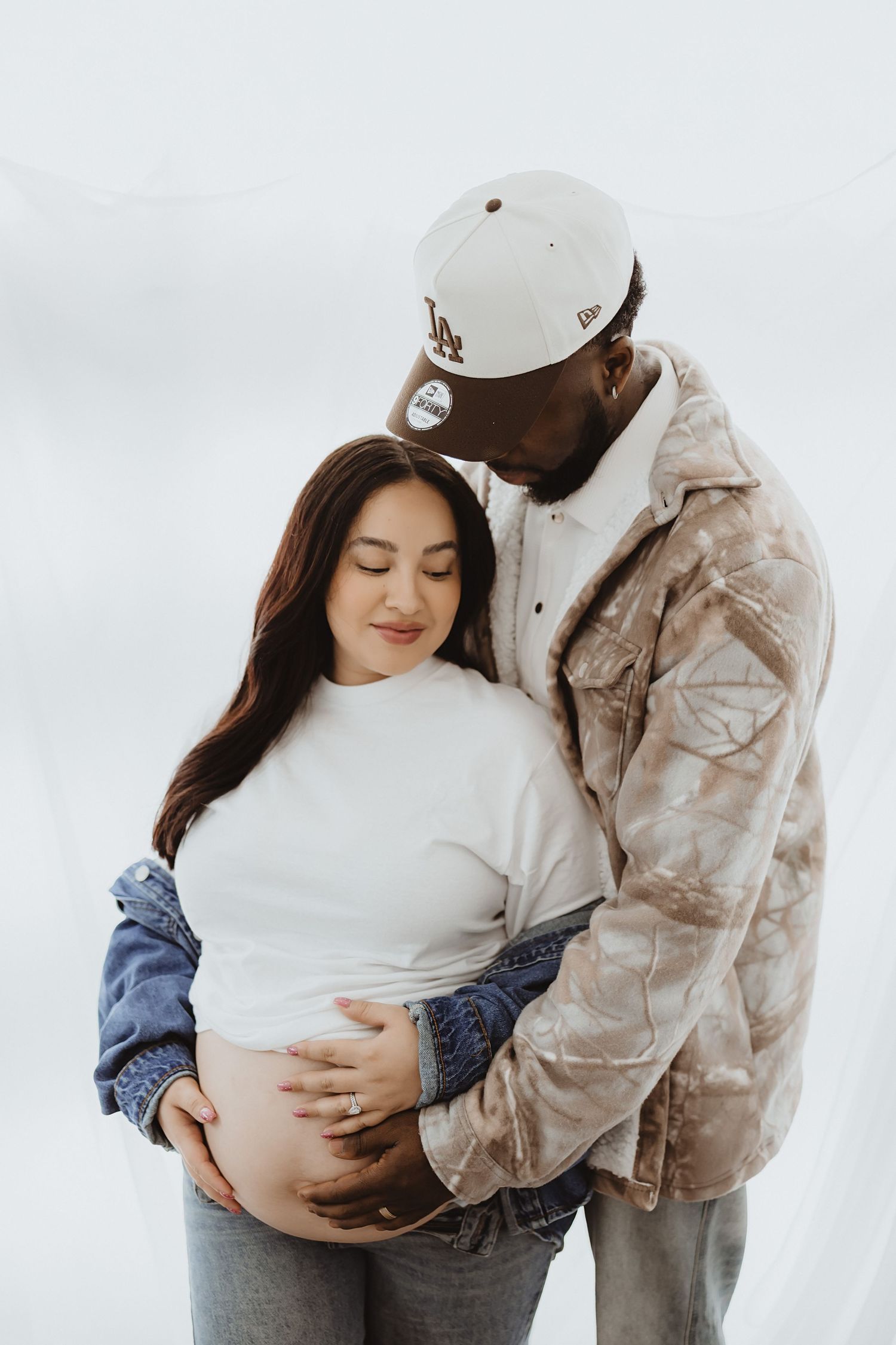 Loving interracial couple embraces during maternity shoot, man kisses pregnant womans head while holding her bump.