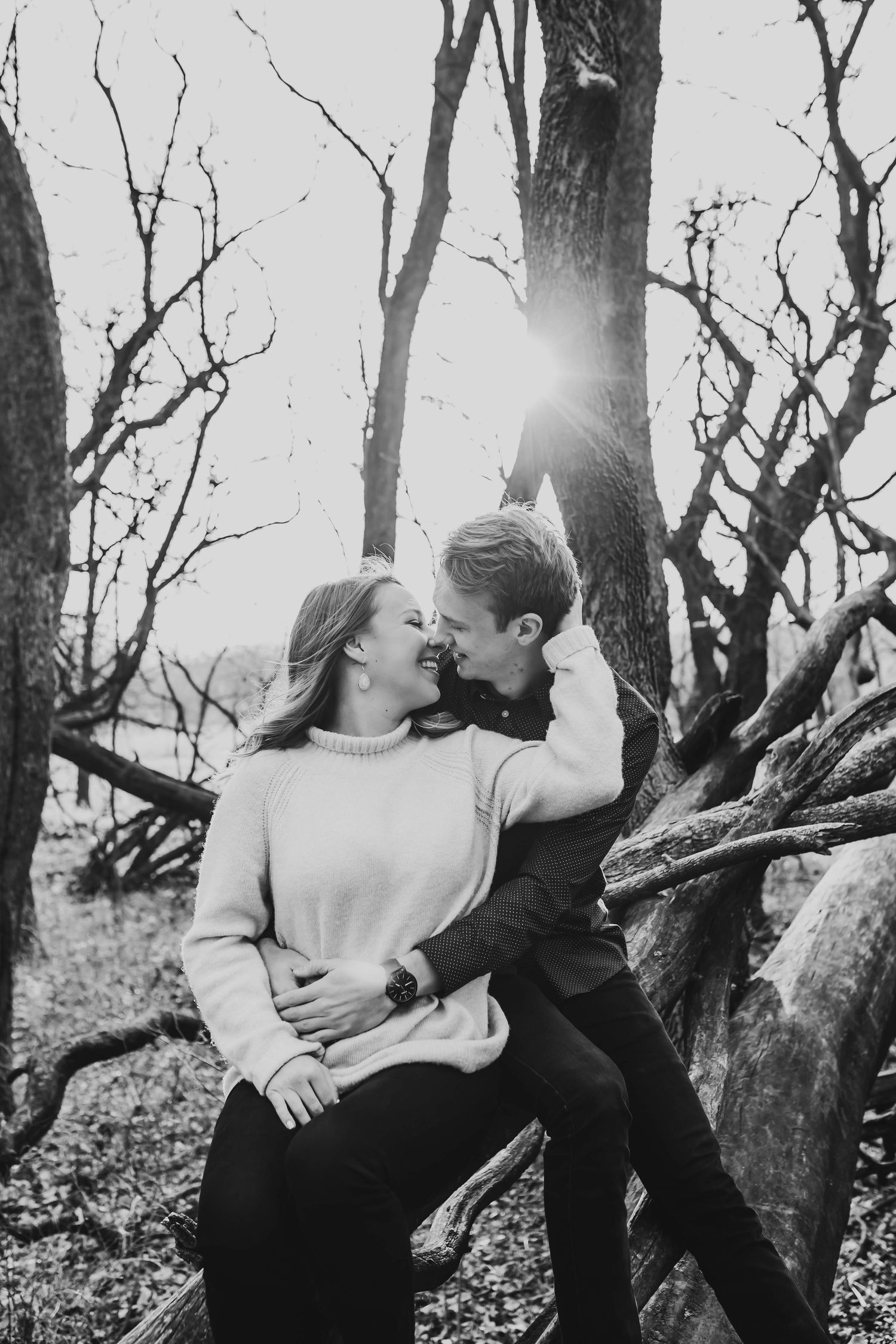 Romantic black and white photo of a couple sharing a tender moment among bare winter trees in a forest.