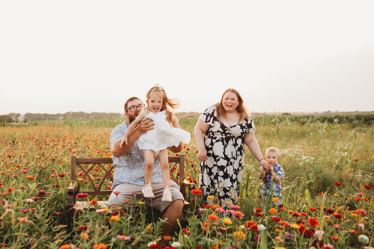 A joyful family of four plays in a colorful wildflower field at golden hour sunset.