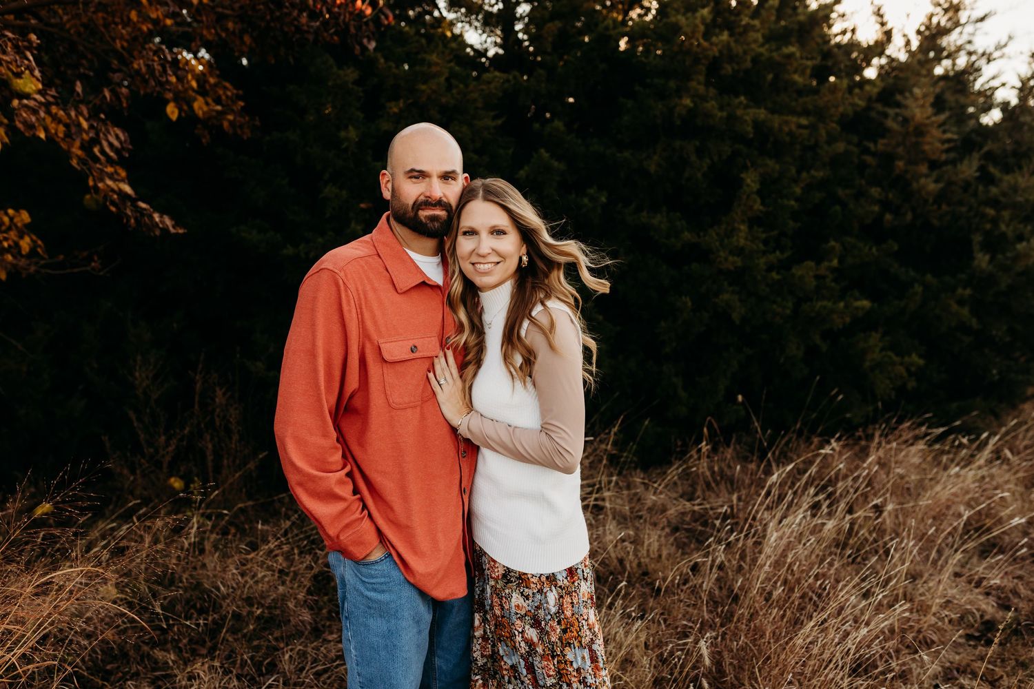Couple embracing in a field with autumn foliage at golden hour.