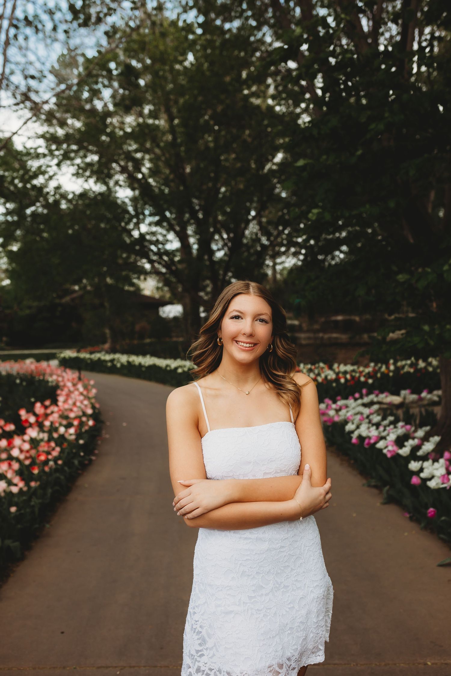 Smiling senior girl in white lace dress standing in a beautiful flower garden.
