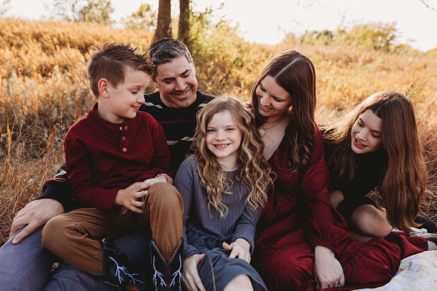 Joyful family of five sitting together on blanket in autumn field laughing and smiling.