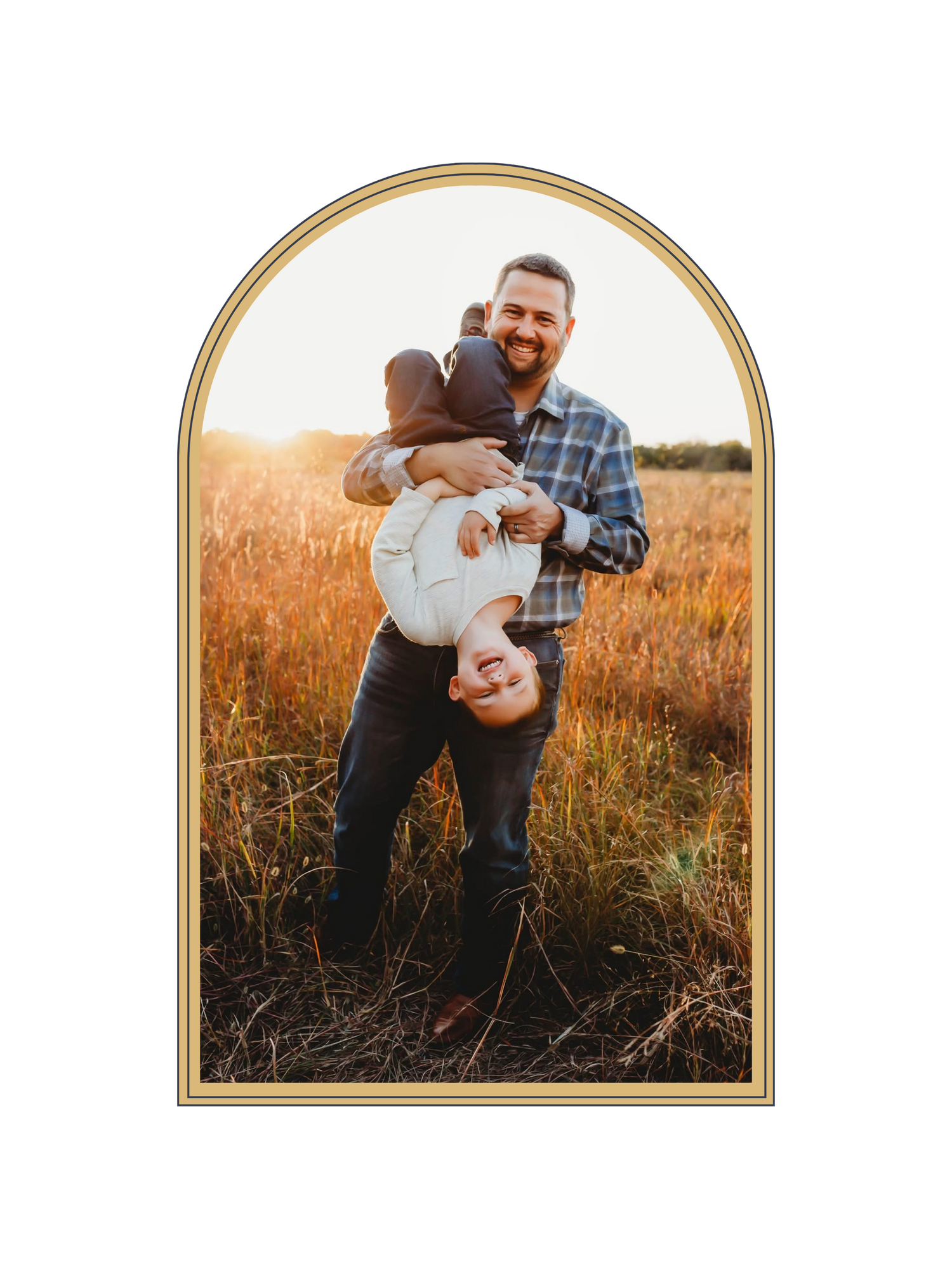A smiling father holds his young child upside down in a golden sunlit field during an outdoor family photo session.