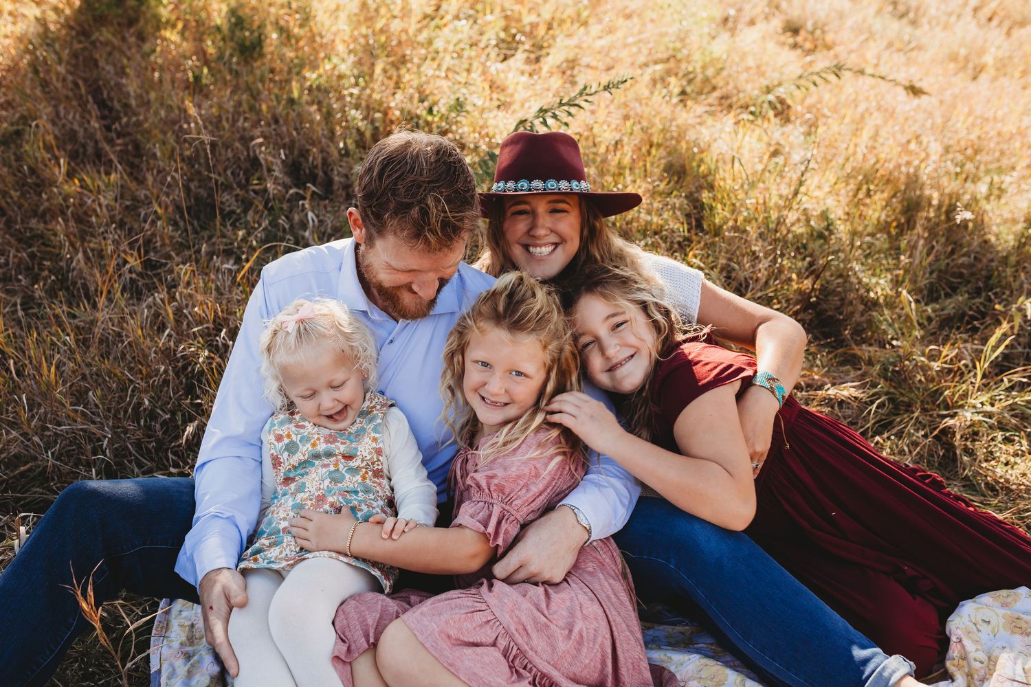 Happy family of five embracing in a sunlit autumn meadow.