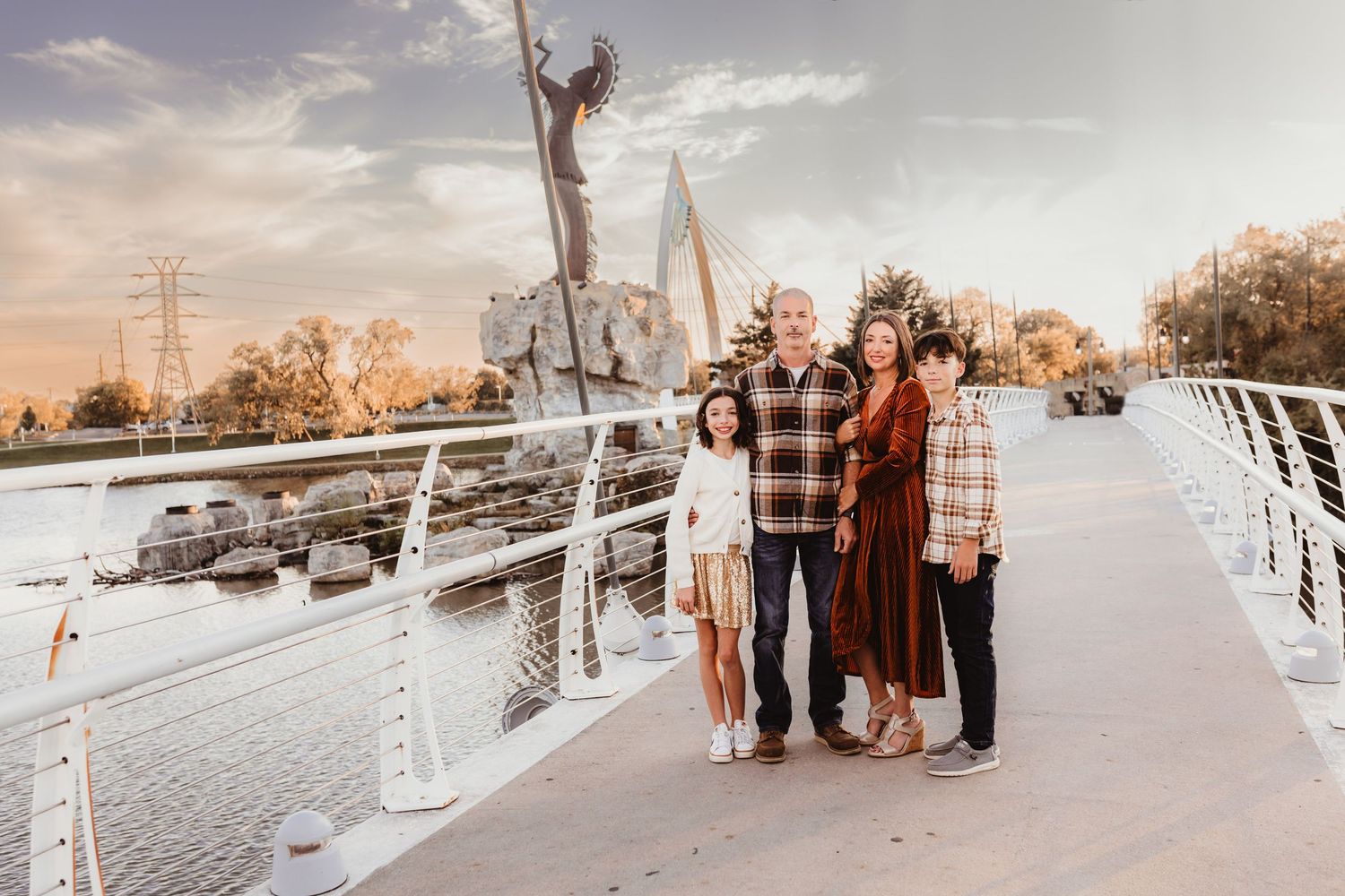 Family of four posing on a bridge with a sunset sculpture backdrop.