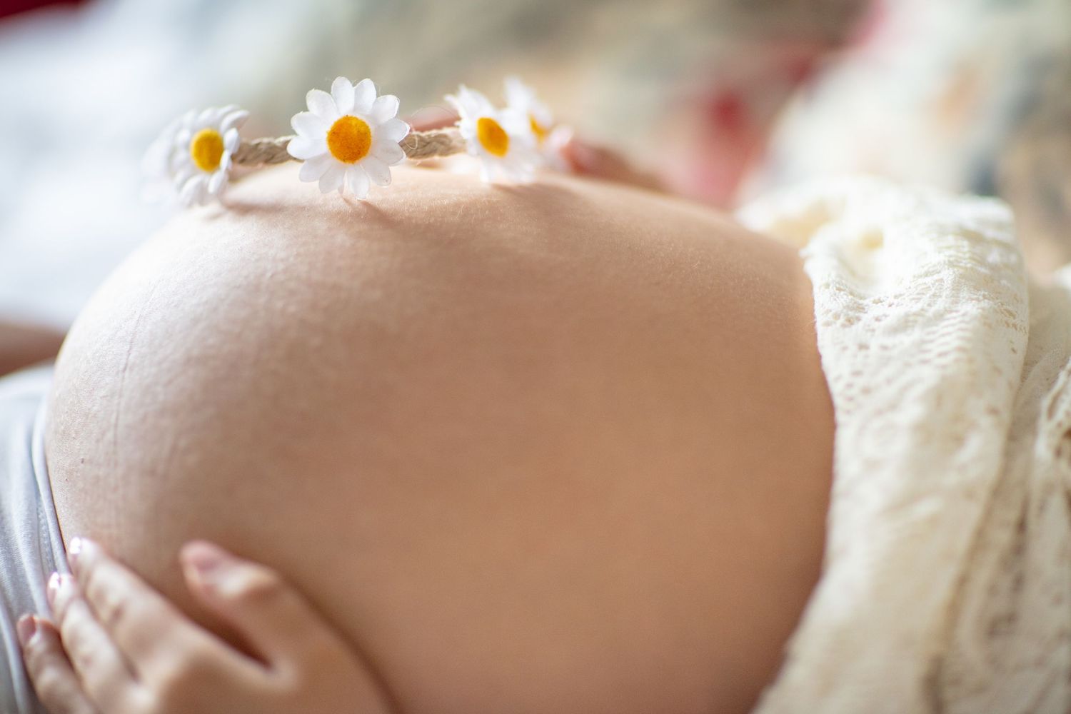 Delicate floral crown resting on maternity bump in soft lighting.