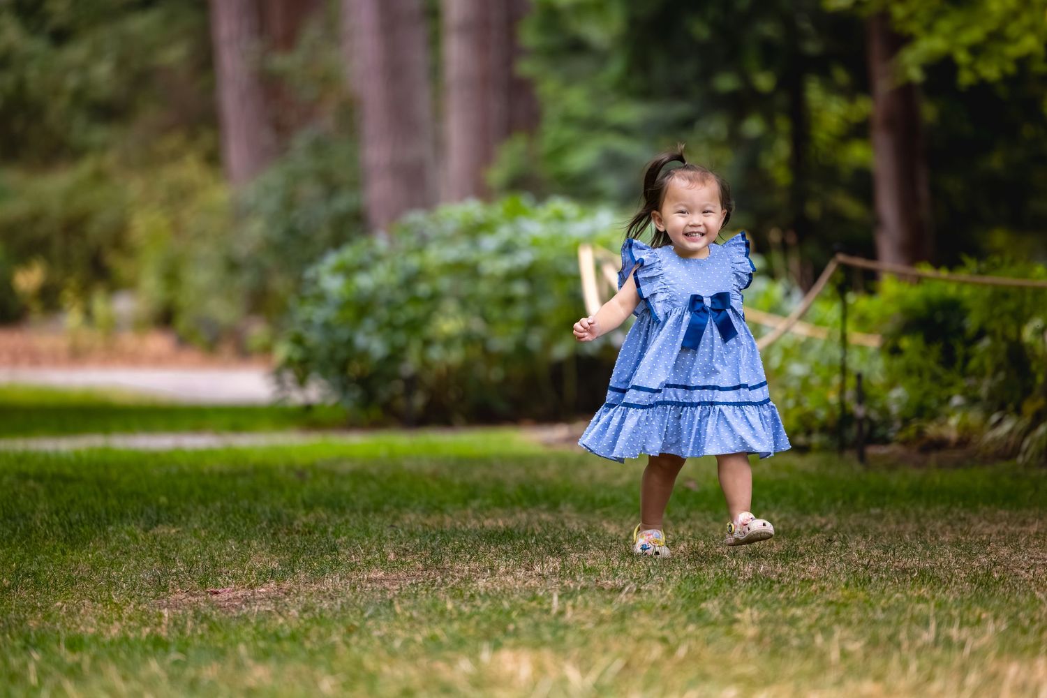 Child in blue ruffled dress playing in a lush green garden setting.