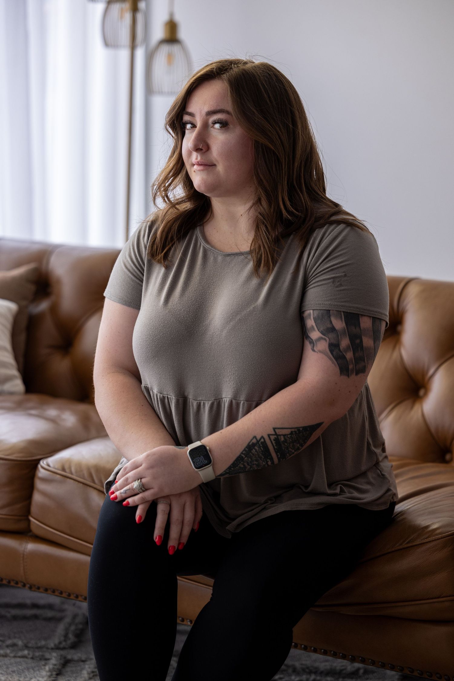 Woman in grey dress sitting casually on brown leather couch.