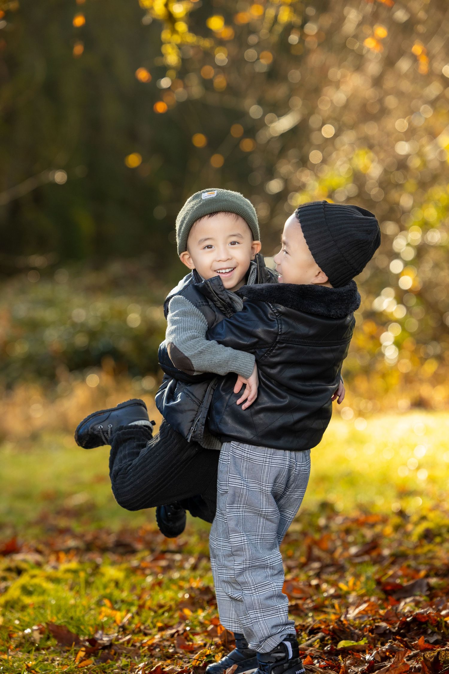Two children play in fallen autumn leaves wearing warm clothes on a golden-lit afternoon.