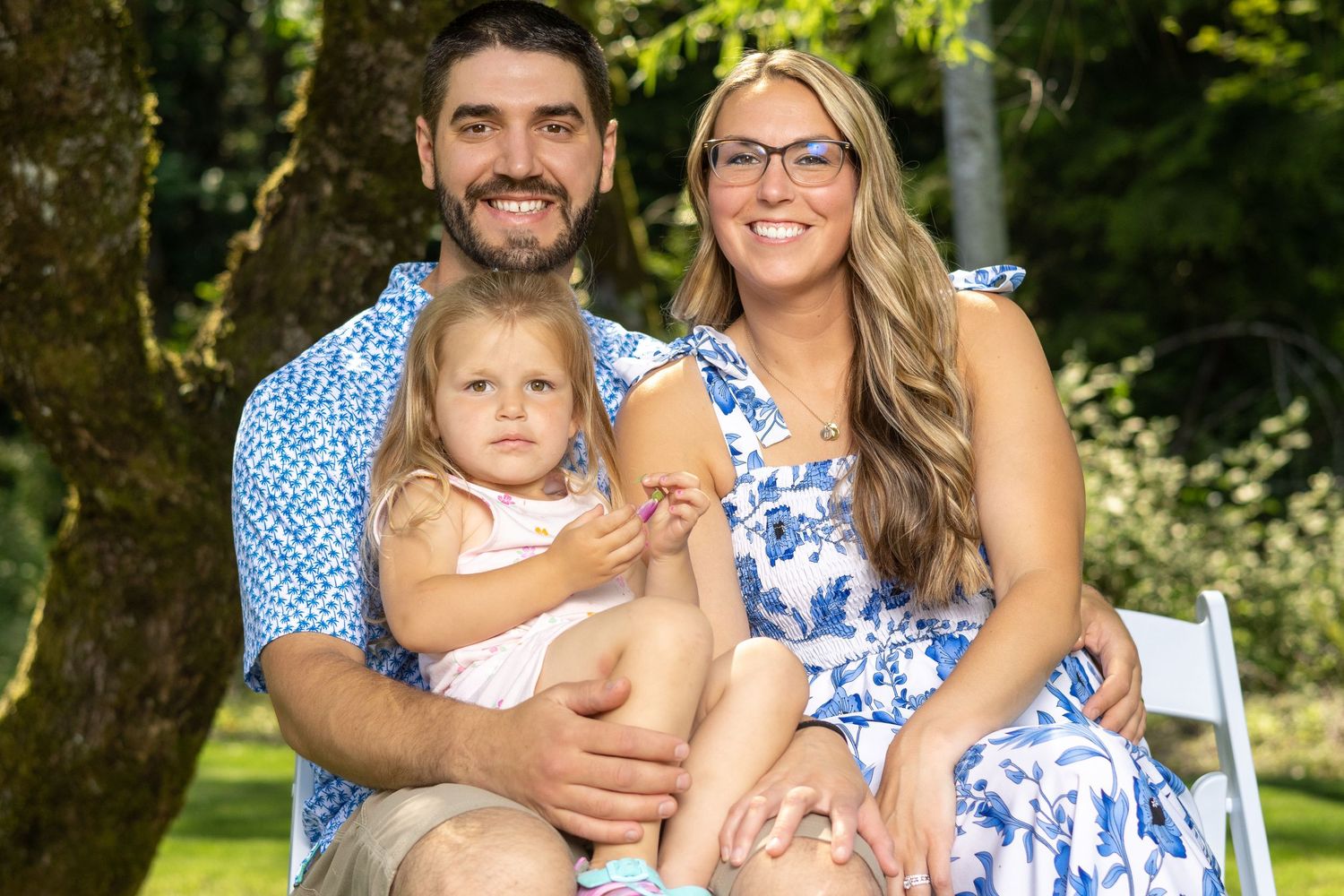 Family in coordinating blue and white outfits smiles together in sunny garden setting.