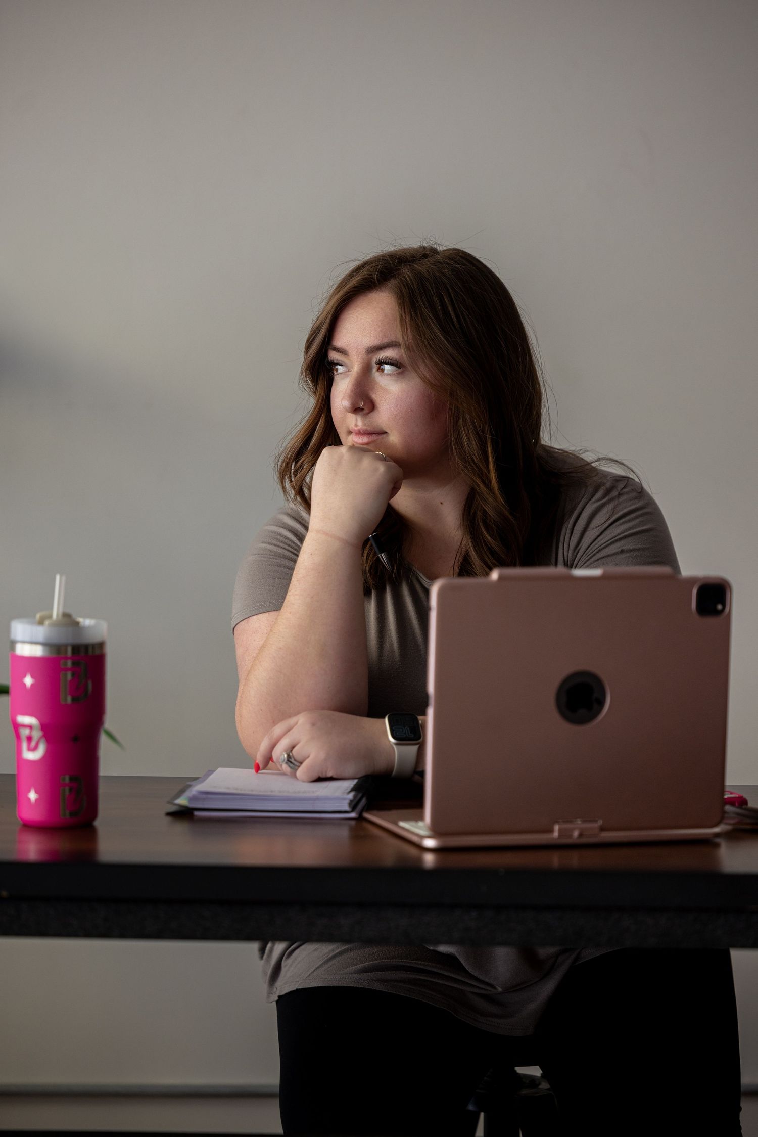 Person working at desk with laptop and pink drink cup in dim lighting.