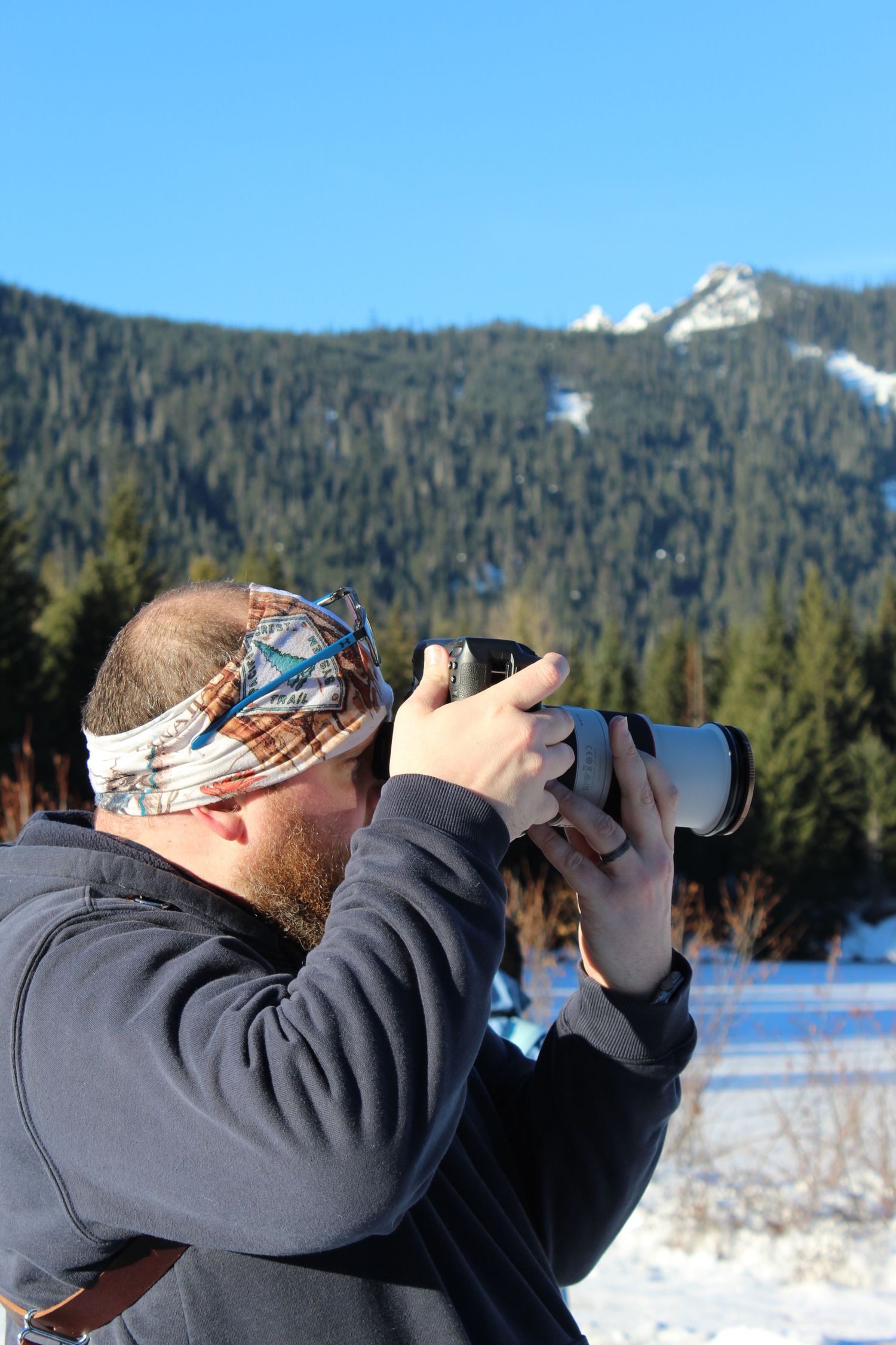 Photographer with telephoto lens capturing shots in snowy mountain landscape.