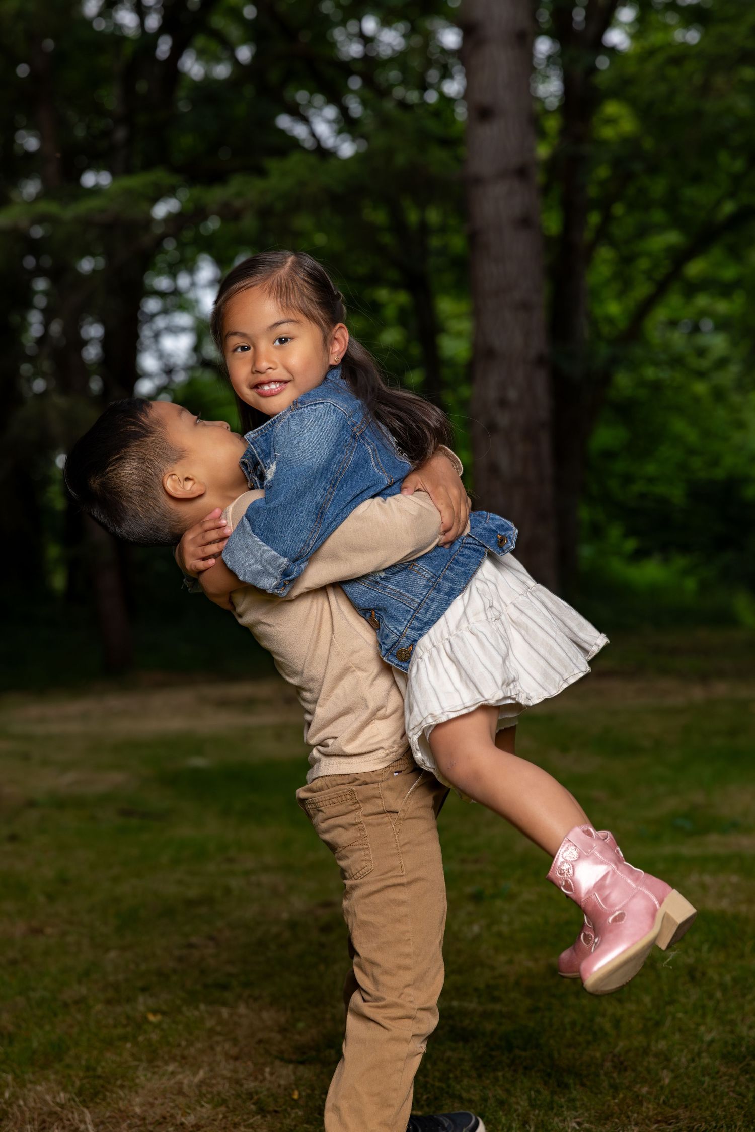 Two children play and laugh together outdoors, with one lifting the other in a playful moment.