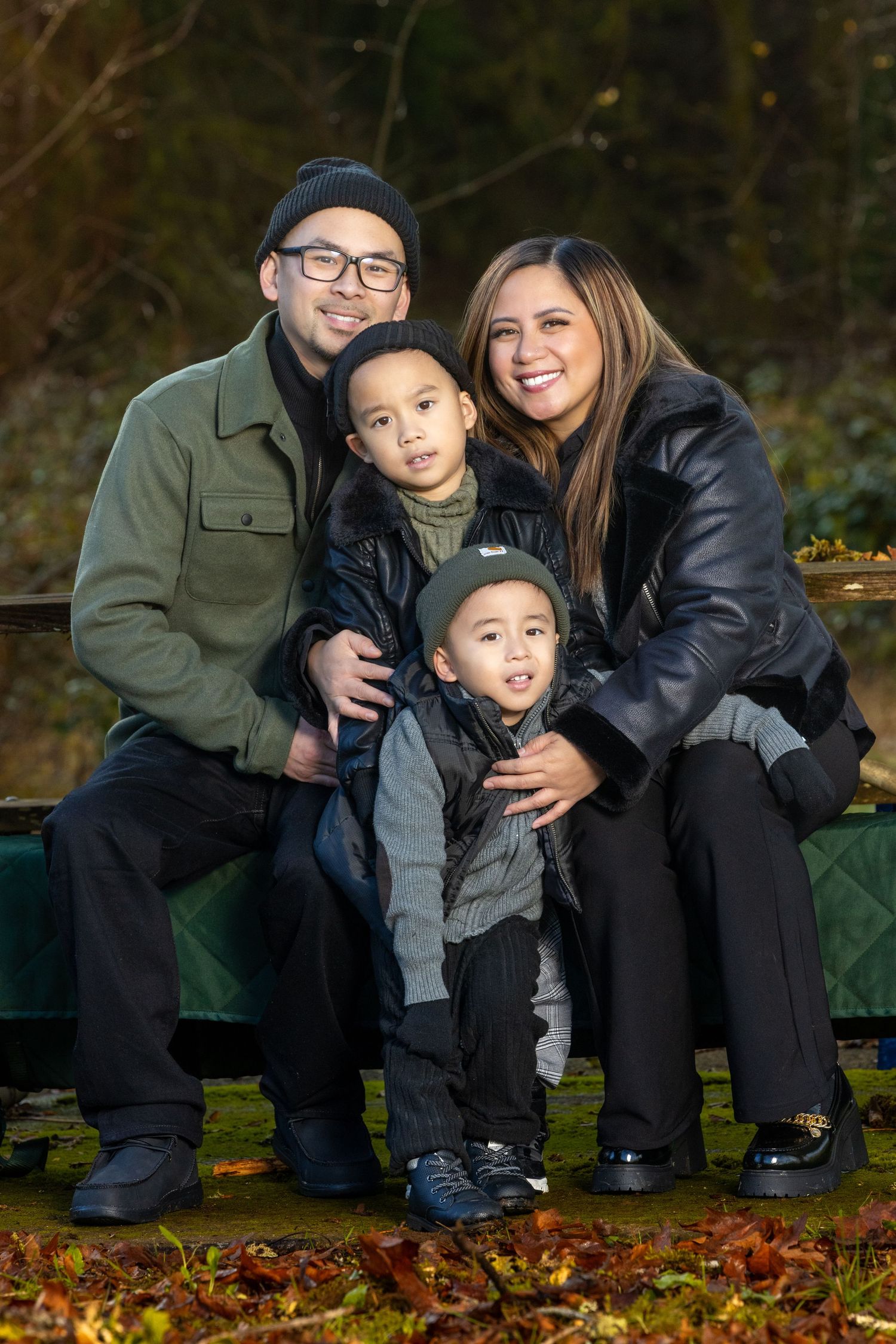 Family of four posing together on ground covered with fallen leaves in autumn setting.